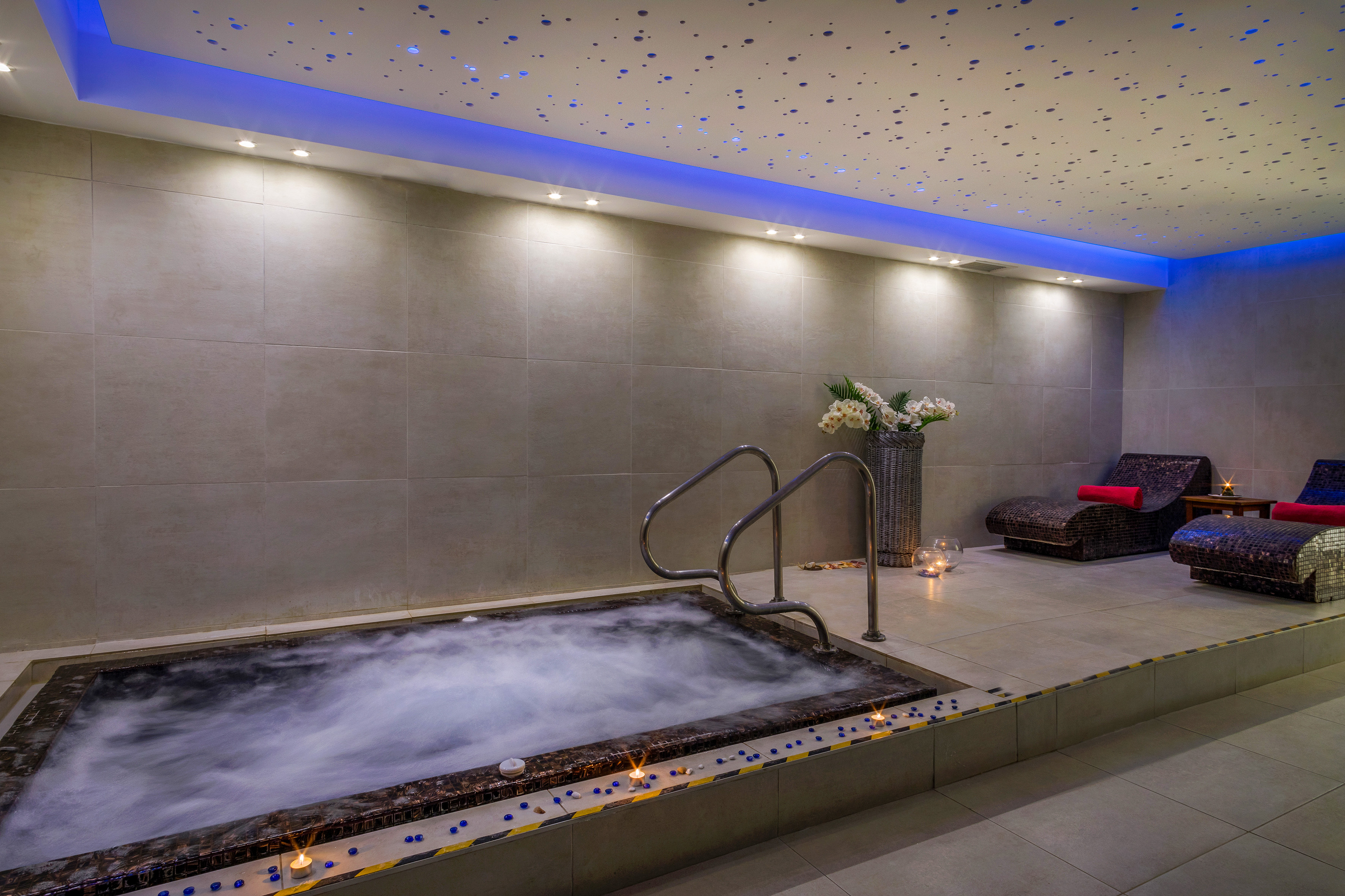 Spa hot tub with blue accent lighting, starry ceiling, and lounge chairs.