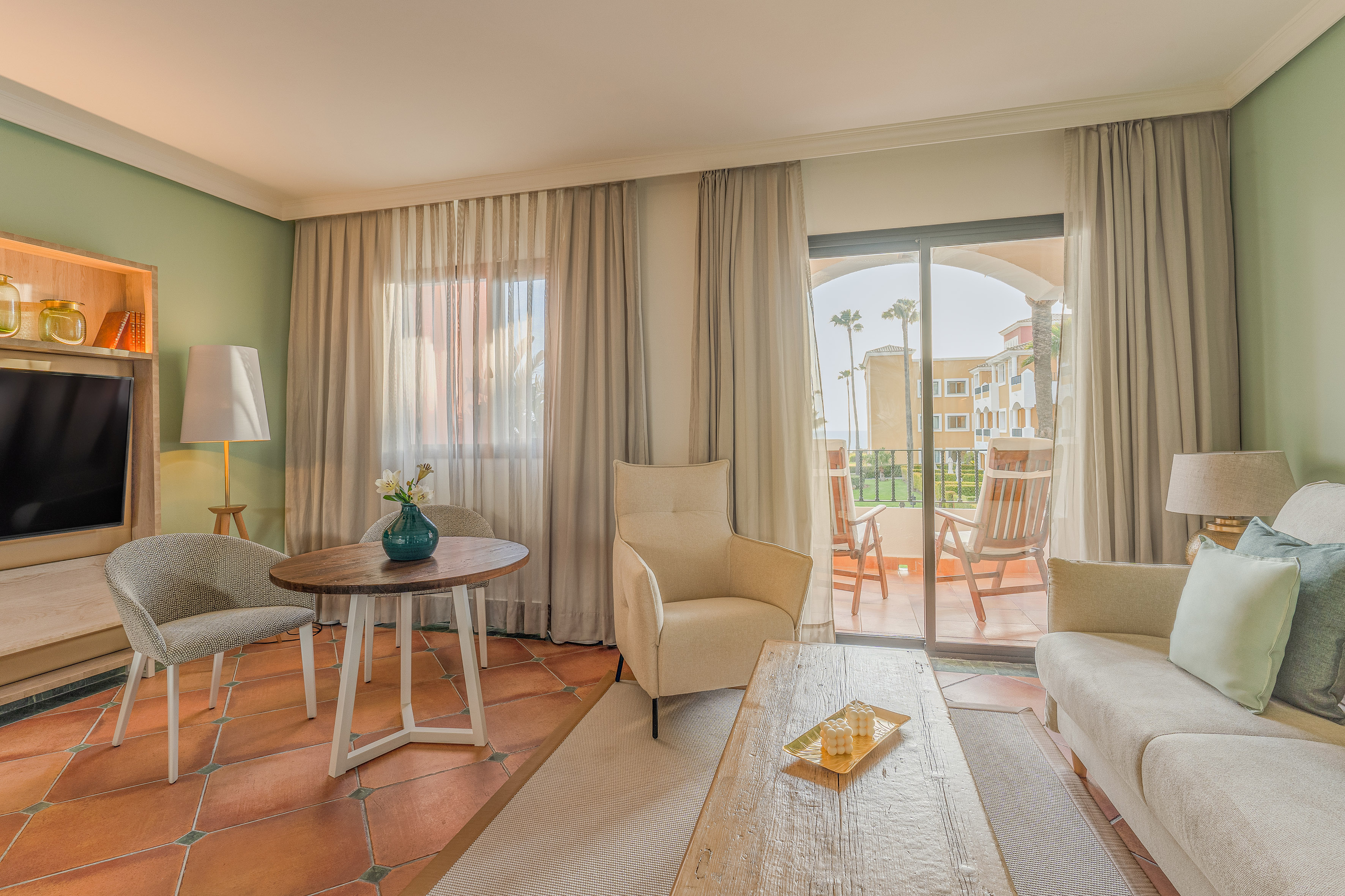 Modern resort living room with sofa, armchairs, coffee table, and balcony access.