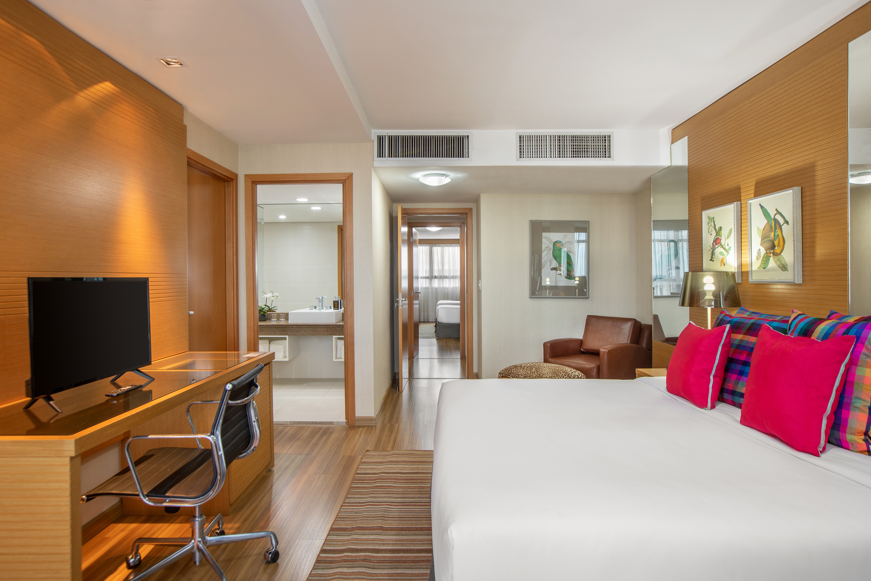 Modern hotel suite with colorful bed, wooden desk, TV, and ensuite bathroom.