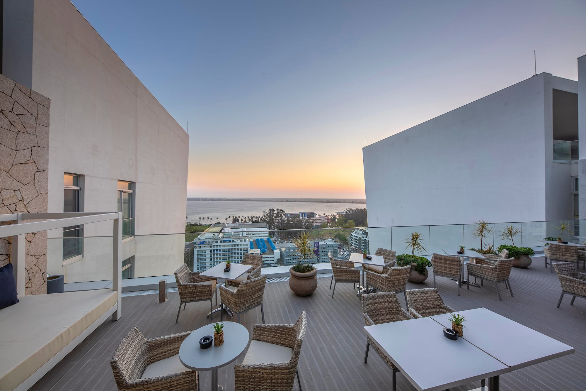 Rooftop lounge with outdoor seating, ocean and city views at sunset.