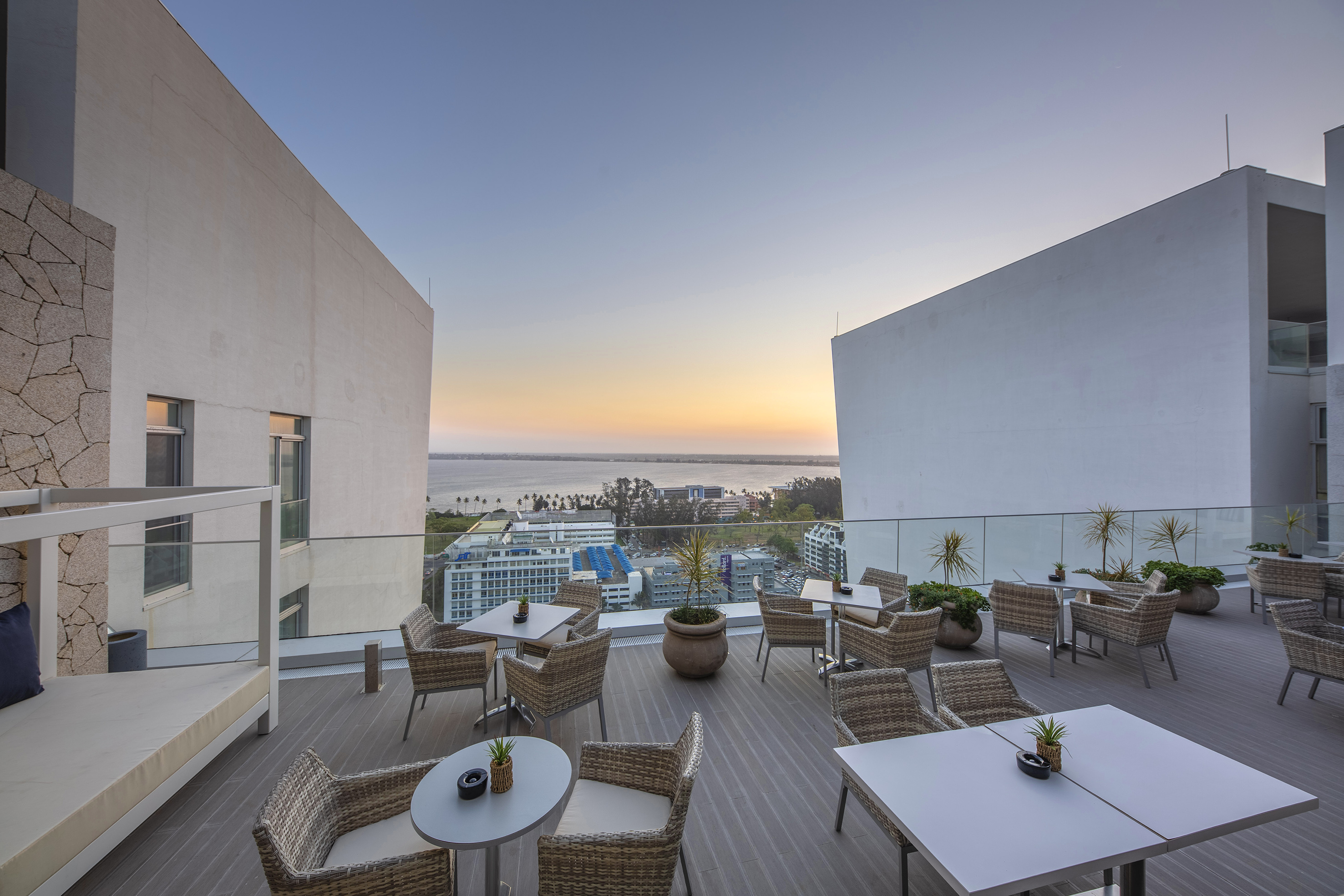 Rooftop lounge with outdoor seating, ocean and city views at sunset.