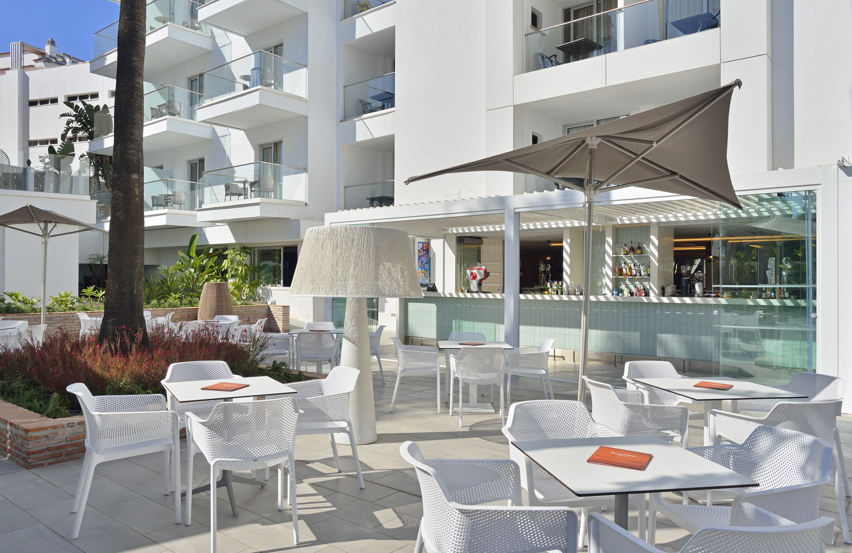 Hotel outdoor bar patio with white seating, modern building, and palm trees.