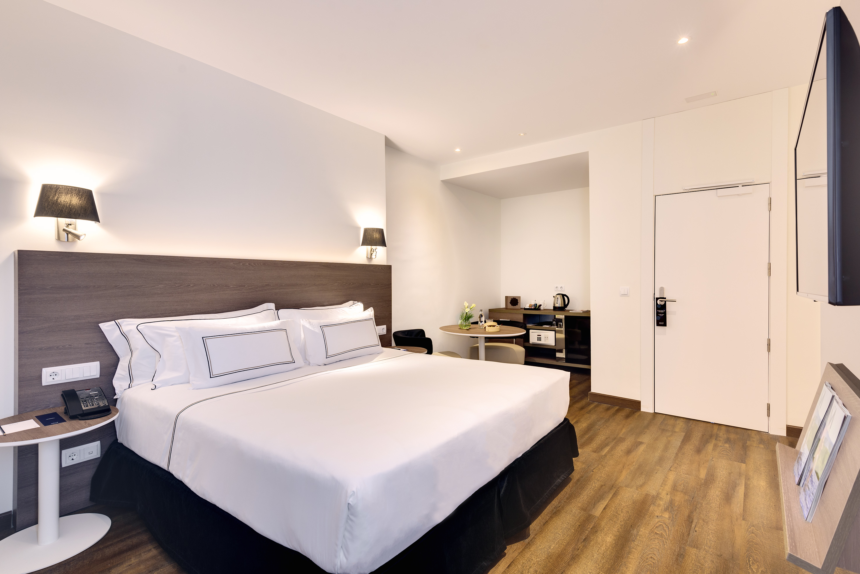 Modern hotel bedroom with king bed, white linens, wood floor, and seating area.