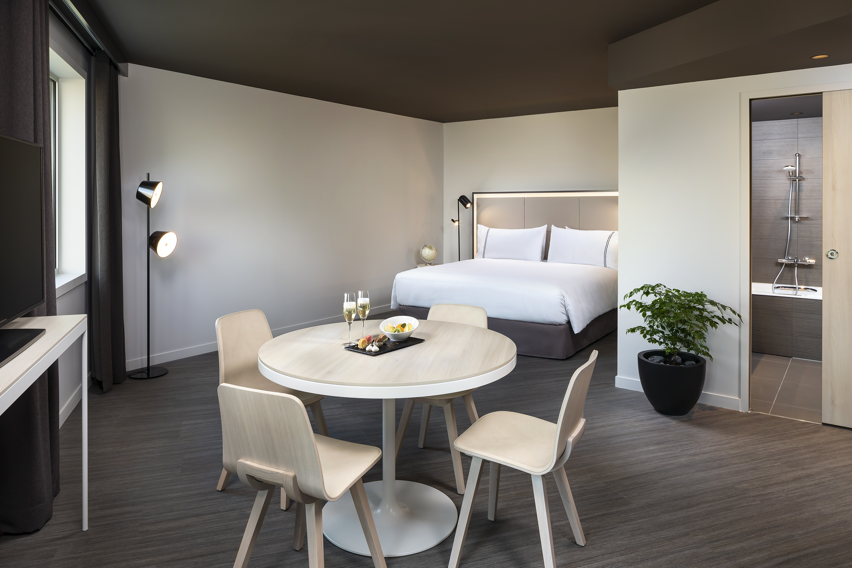 Modern hotel suite with bed, dining table, champagne, and en-suite bathroom.