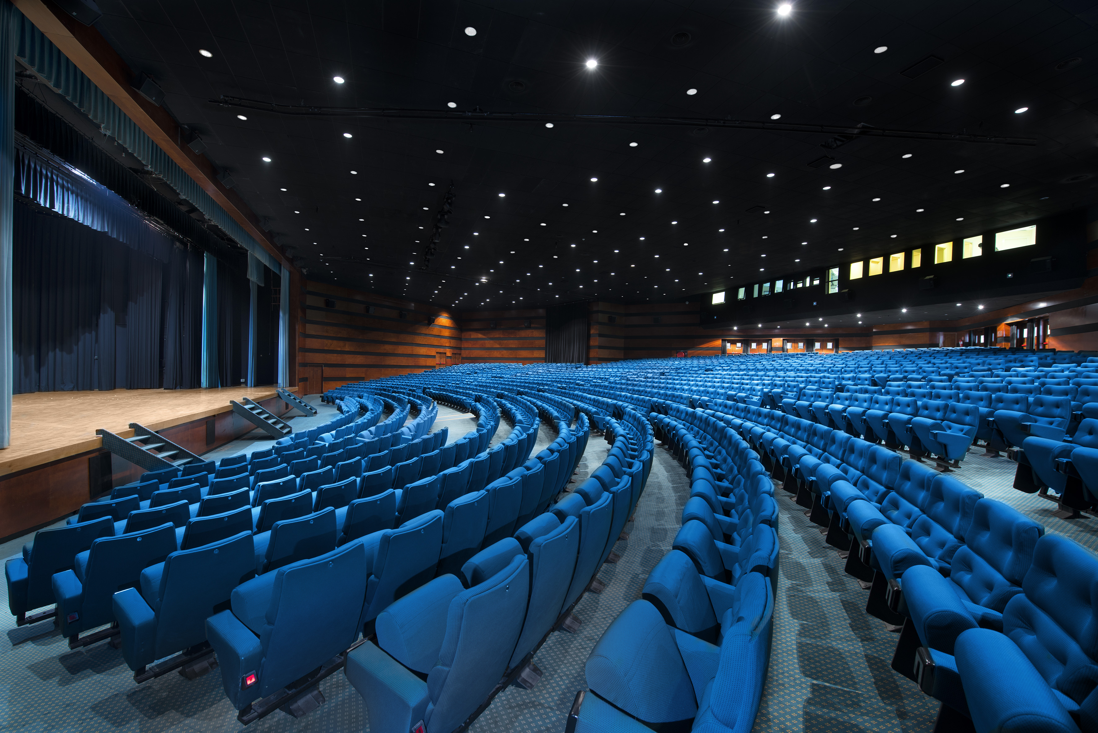 Empty theater auditorium with curving blue seats and a stage.