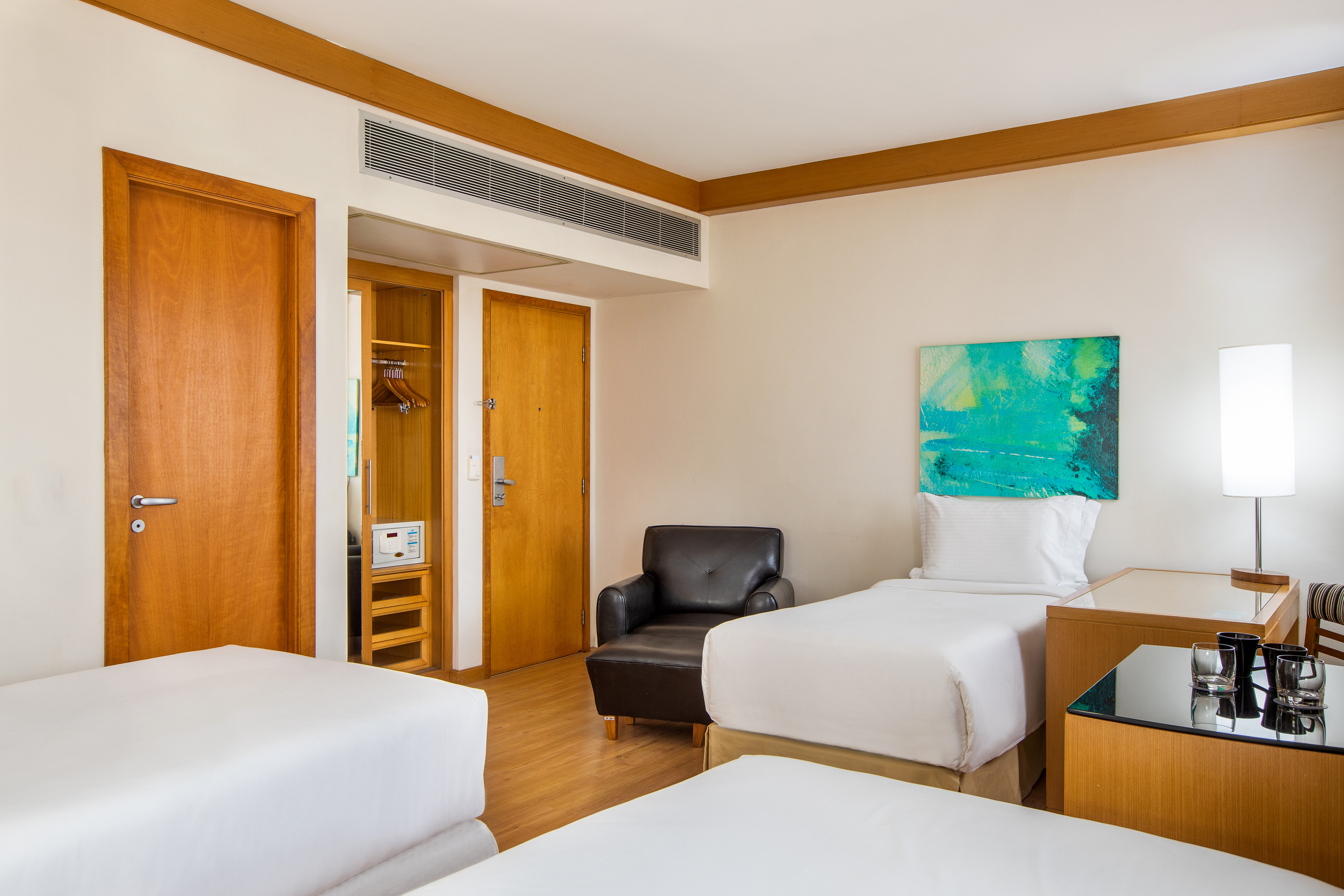Hotel guest room with two twin beds, armchair, and vibrant abstract art.