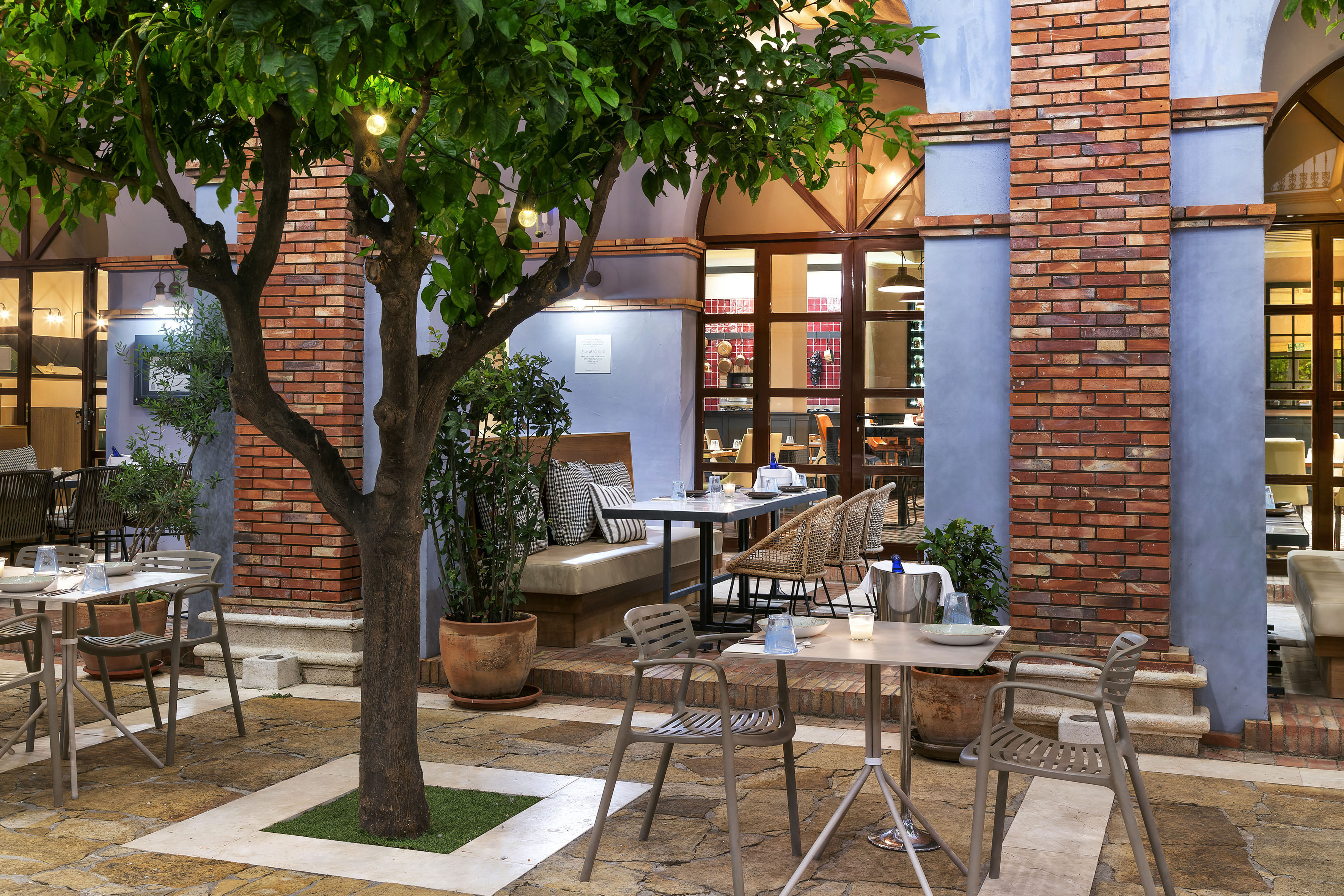 Al fresco restaurant patio with dining tables, green tree, and brick walls.