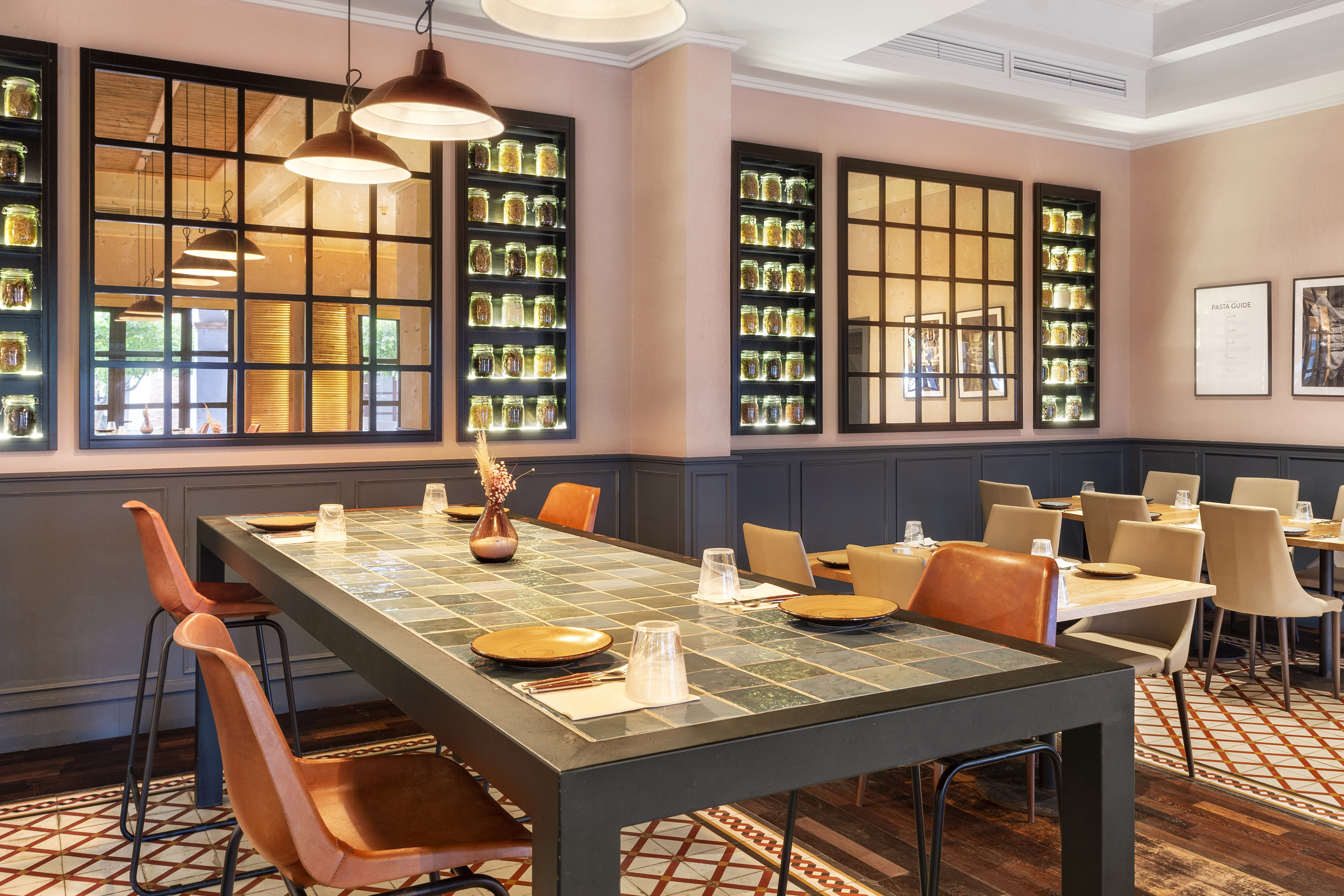 Tiled communal table, leather chairs, and spice jar walls in a restaurant.