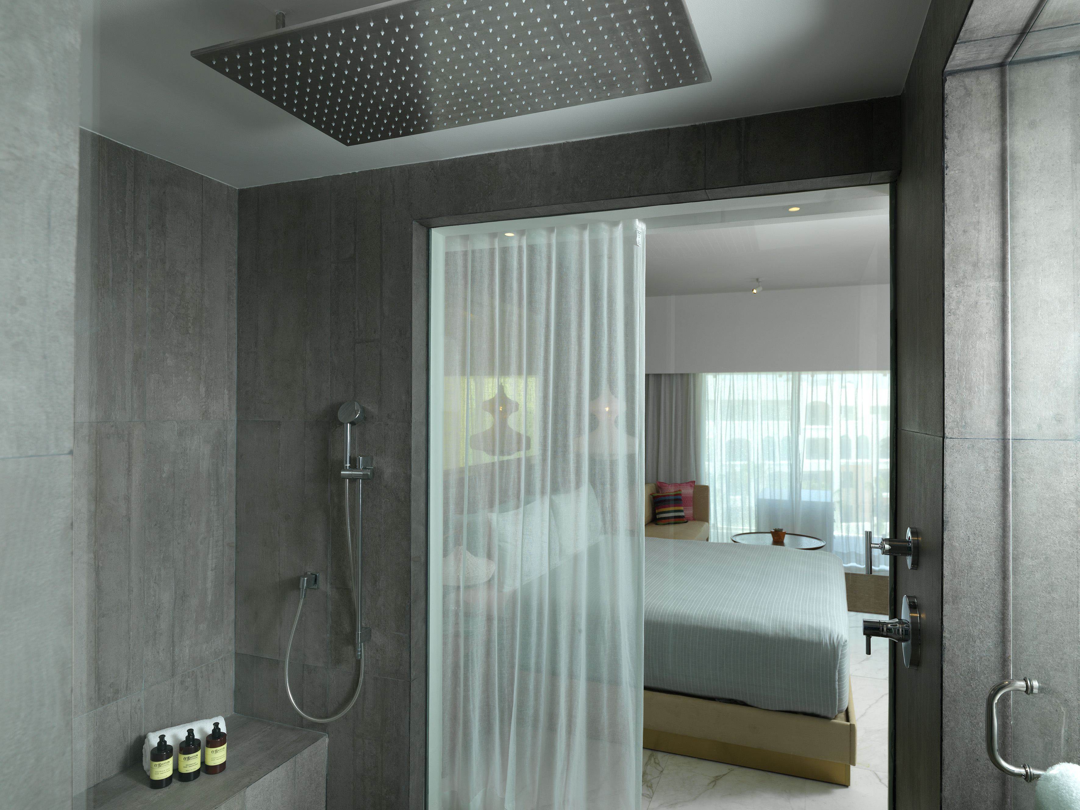 Luxurious grey-tiled shower with rain head, adjacent to a contemporary bedroom.