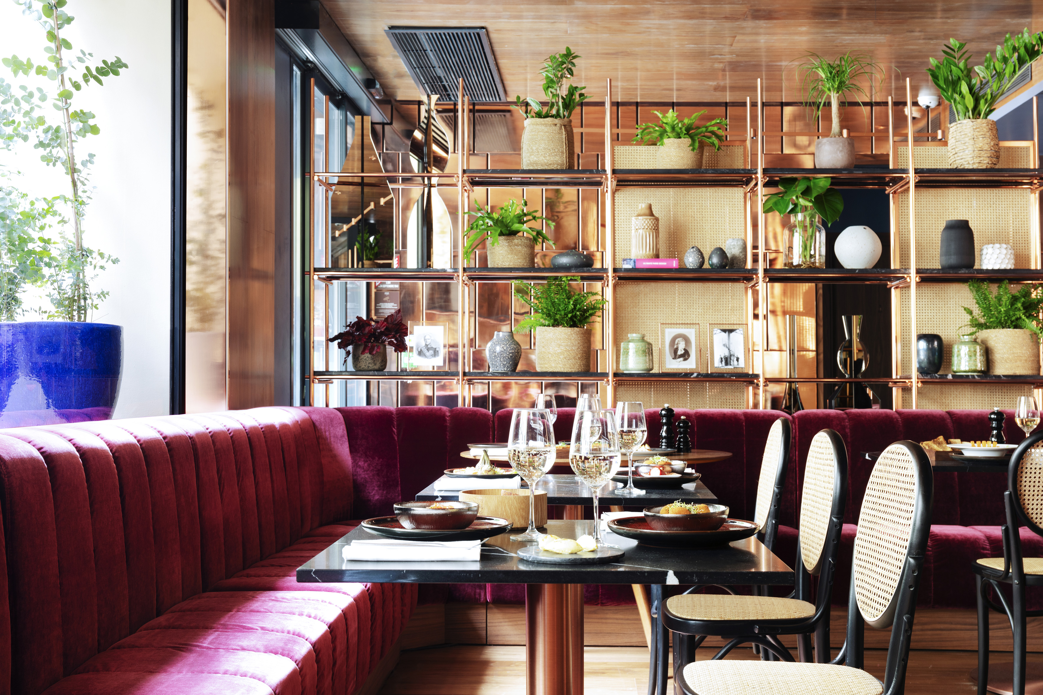 Restaurant dining: red velvet booths, marble tables, copper shelving, plants.