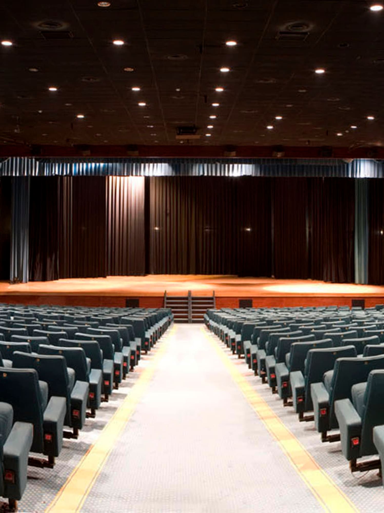 Auditorium interior with empty dark seats, stage, and wood paneling.