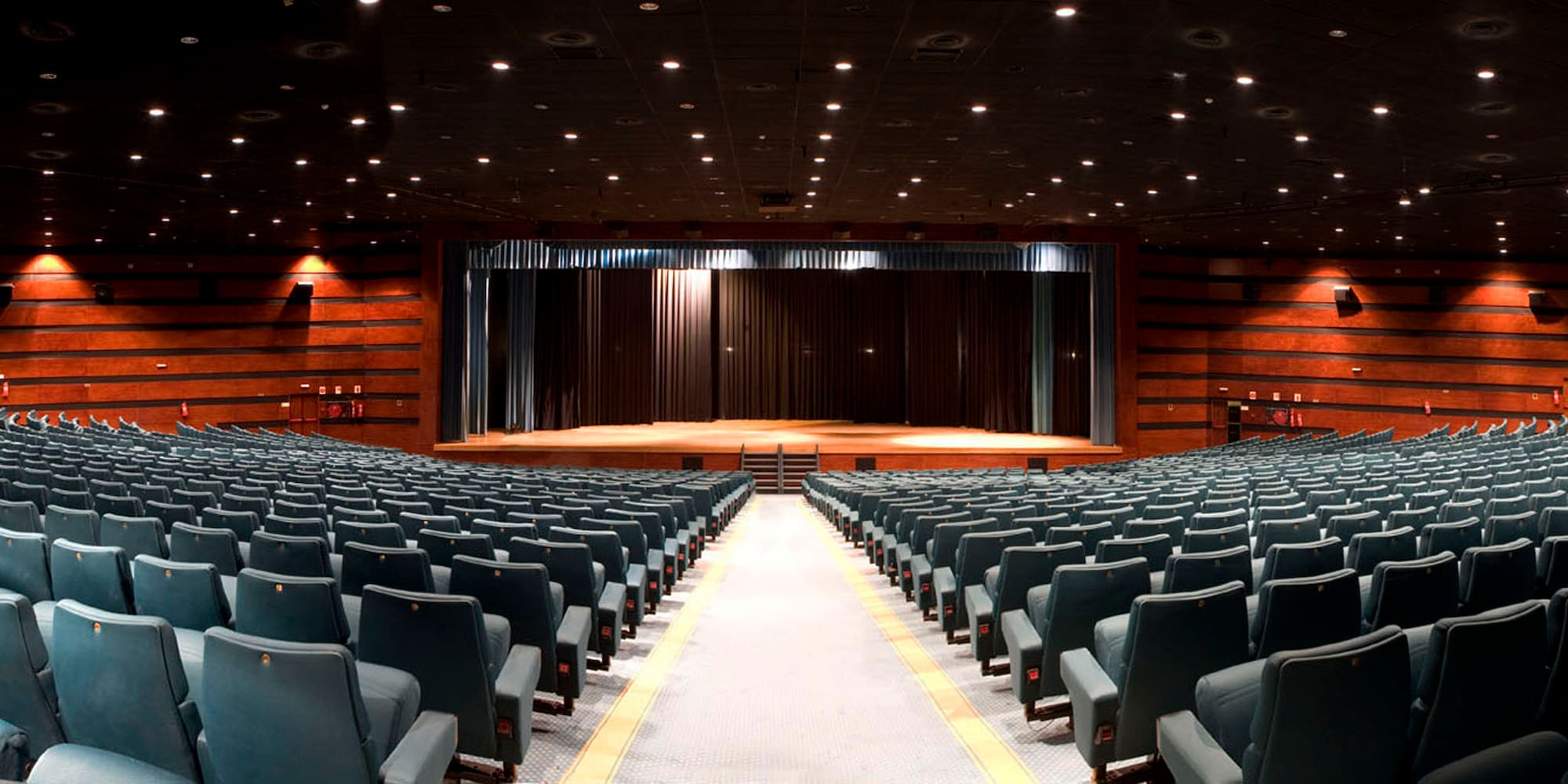Large empty auditorium with dark seats, wooden panels, and a proscenium stage.