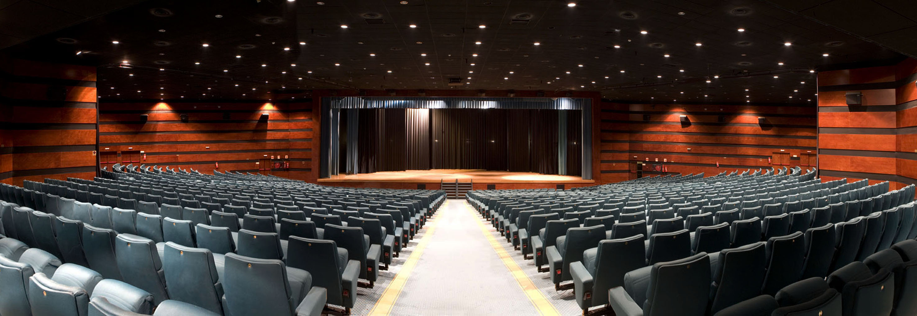 Large empty auditorium with dark seats, wooden panels, and a proscenium stage.