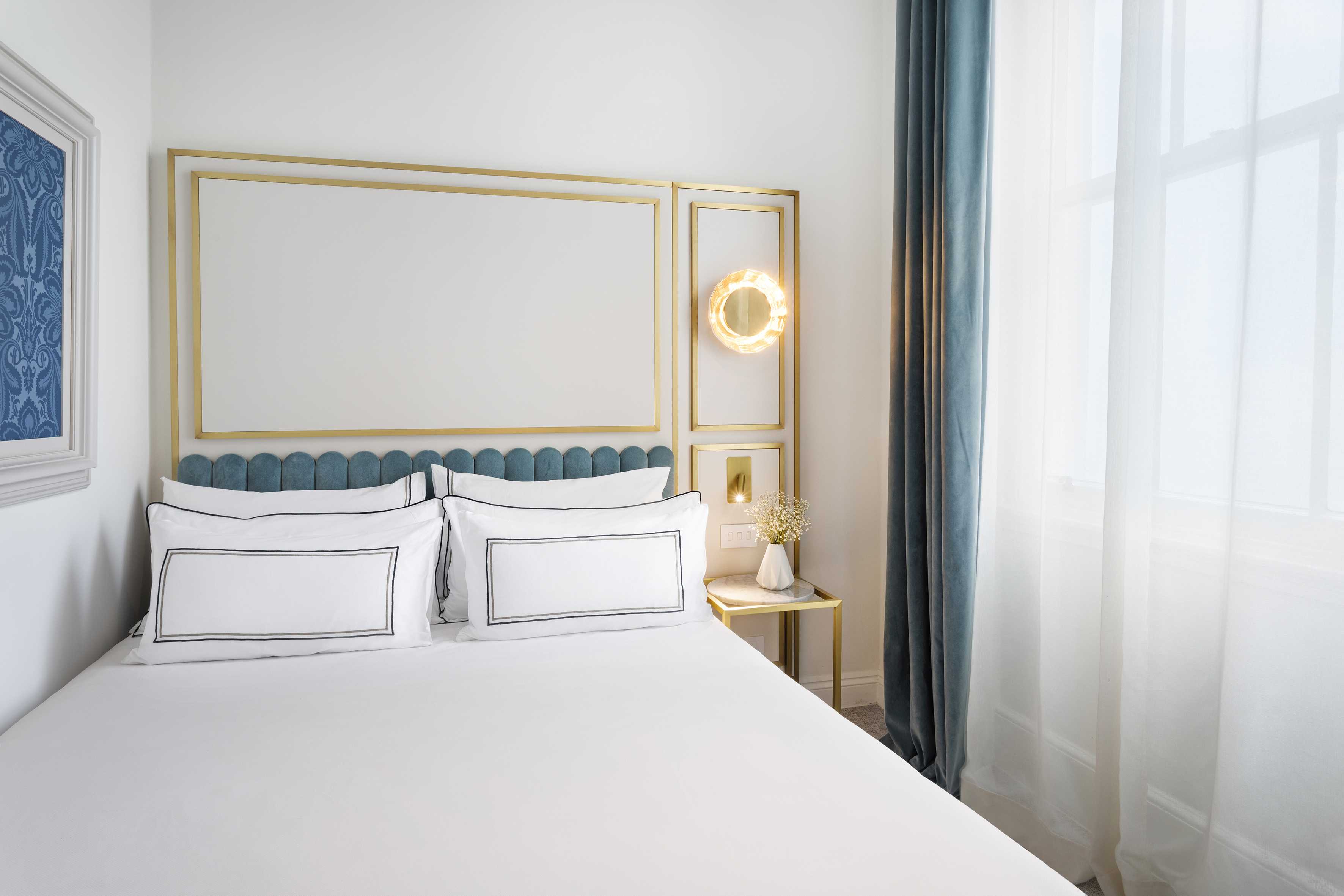 Bright modern bedroom with white bed, blue scalloped headboard, and gold accents.