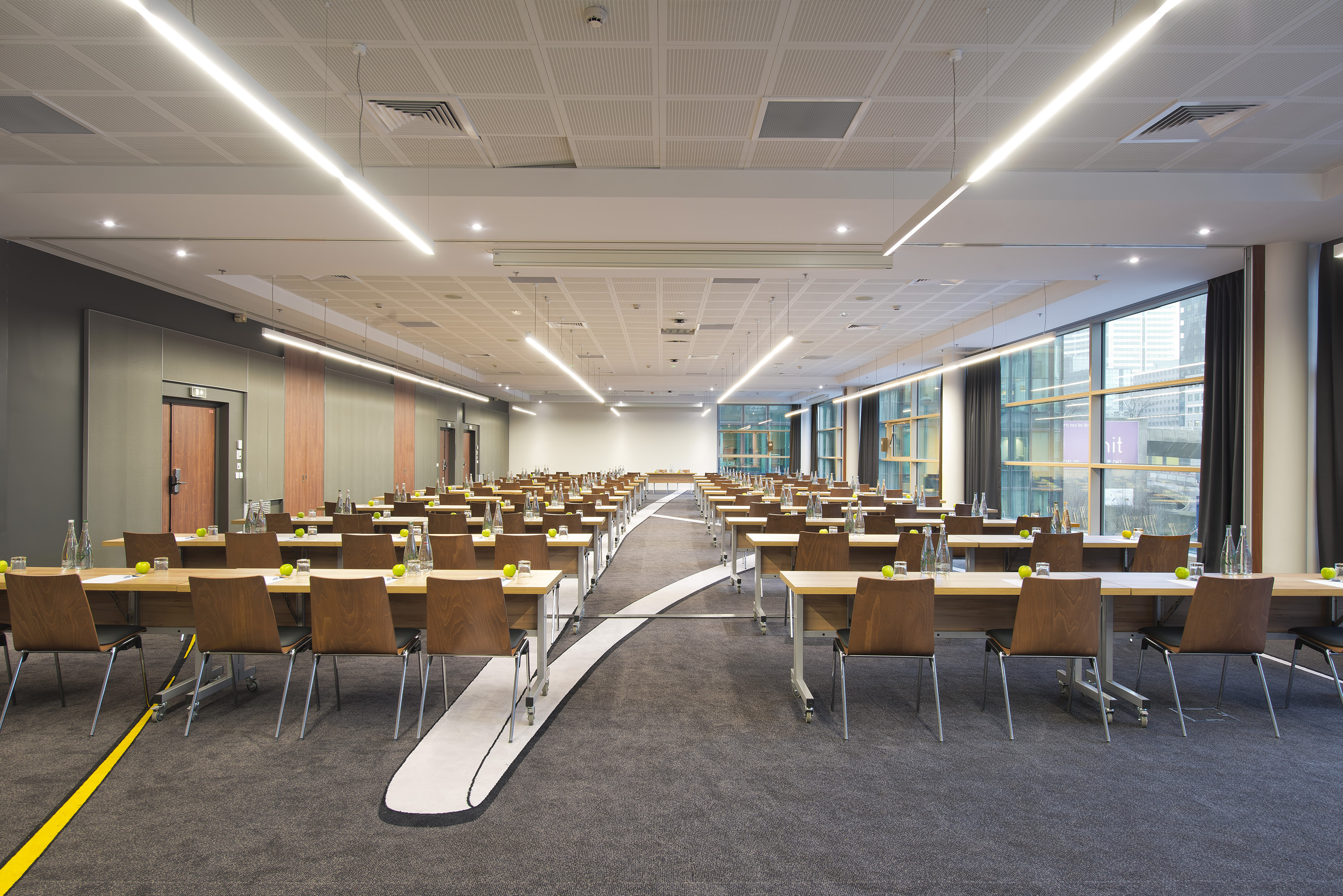 Modern conference room setup with tables, chairs, linear lighting, and windows.