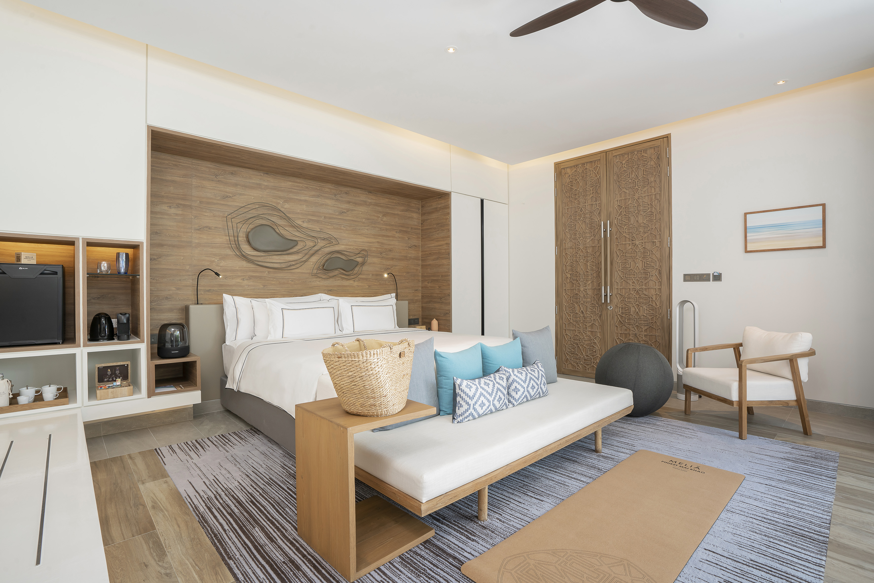 Modern hotel wellness room with king bed, daybed, wood decor, and yoga mat.