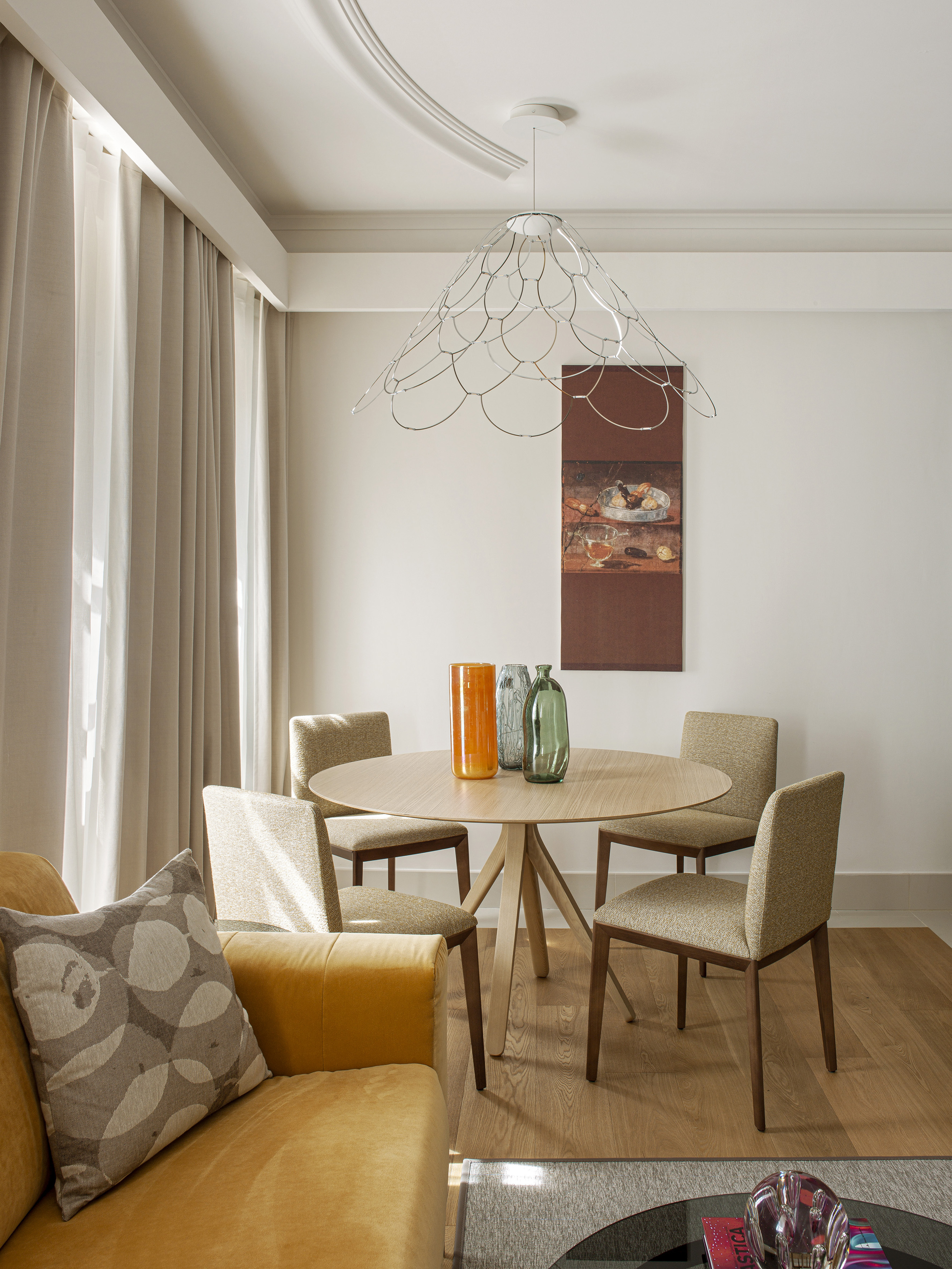 Modern dining area with round wood table, neutral chairs, and wire pendant light.