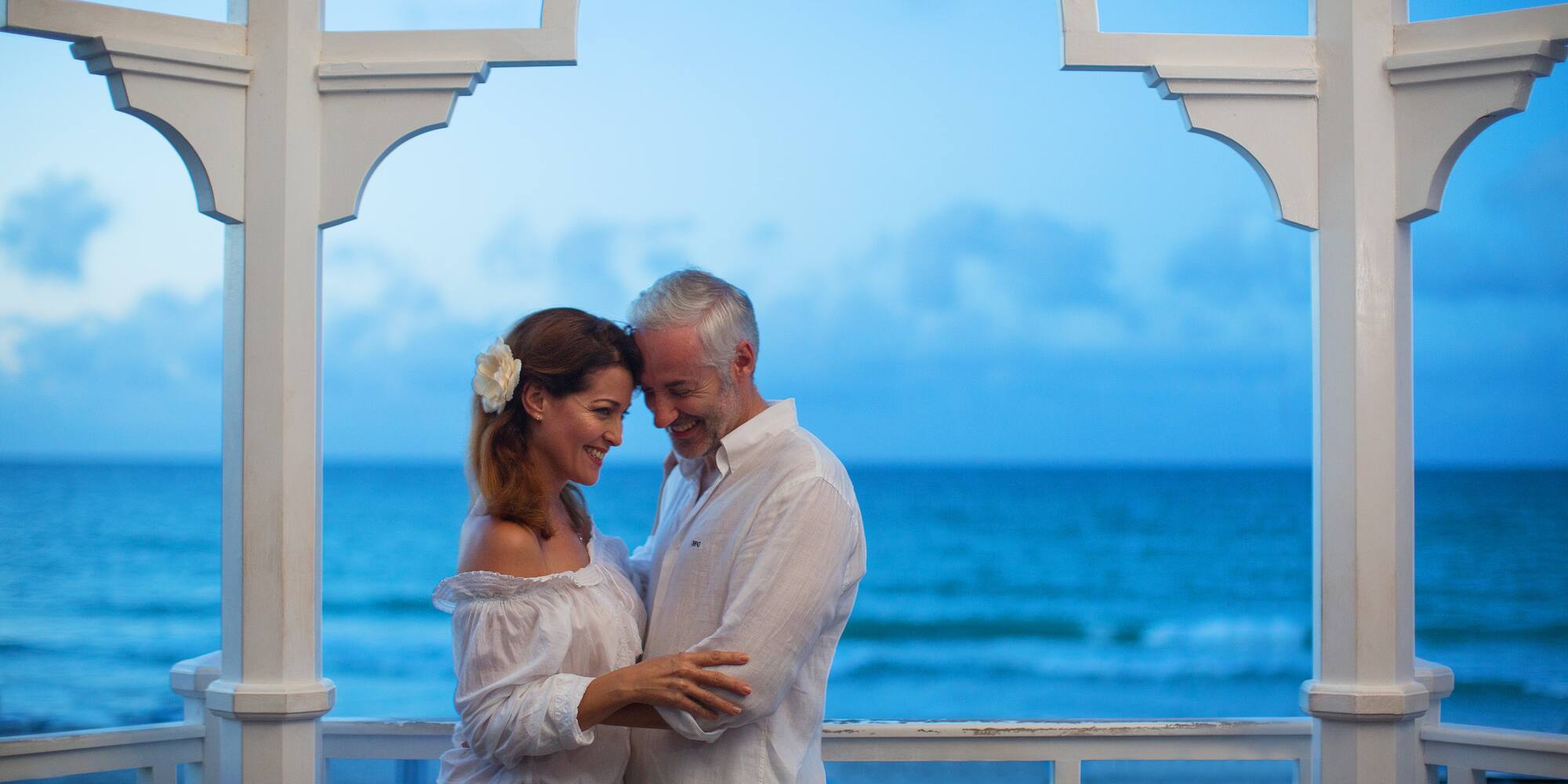 a man and woman standing on a porch with water in the background