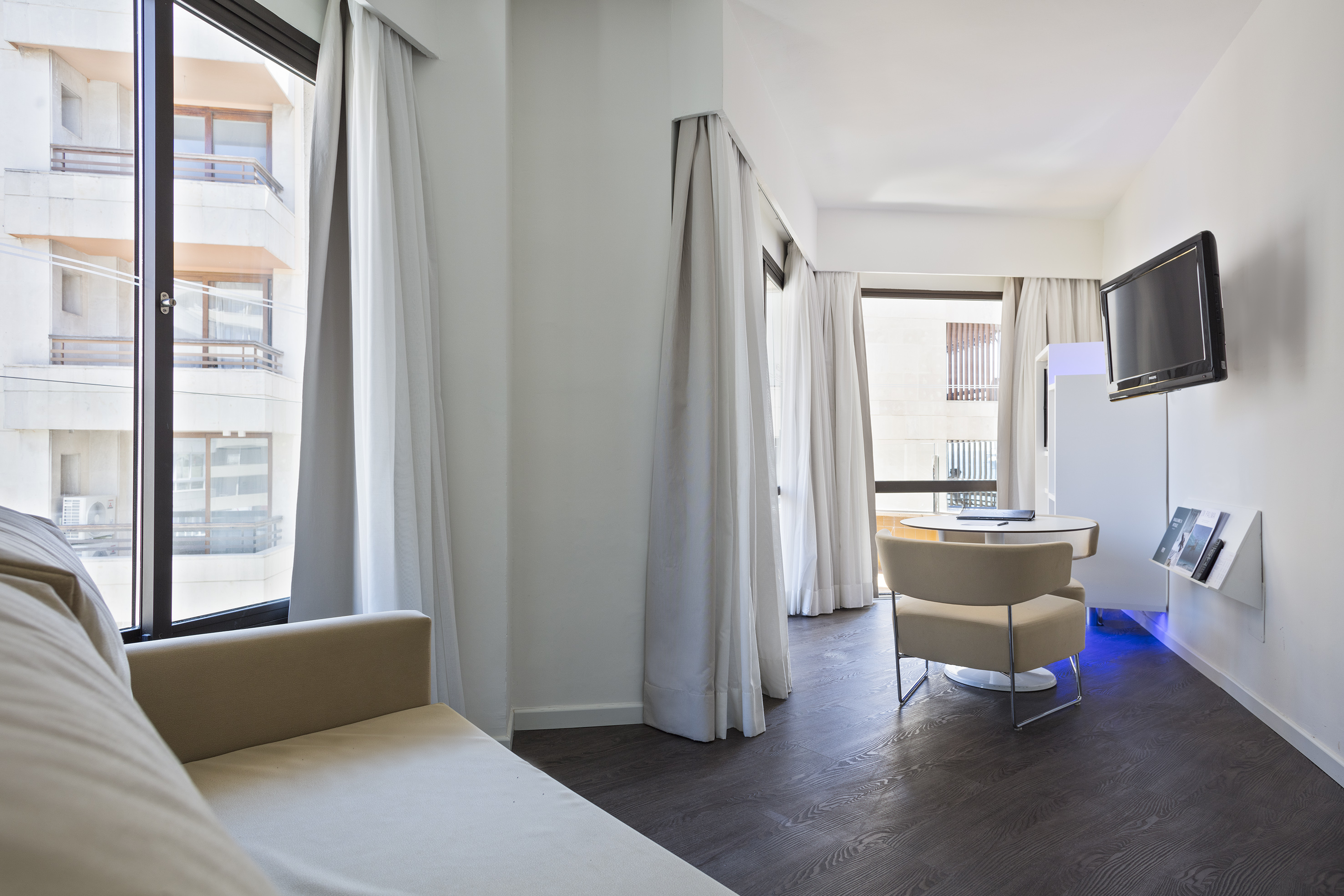 Contemporary hotel suite living space with sofa, TV, table, and city view.