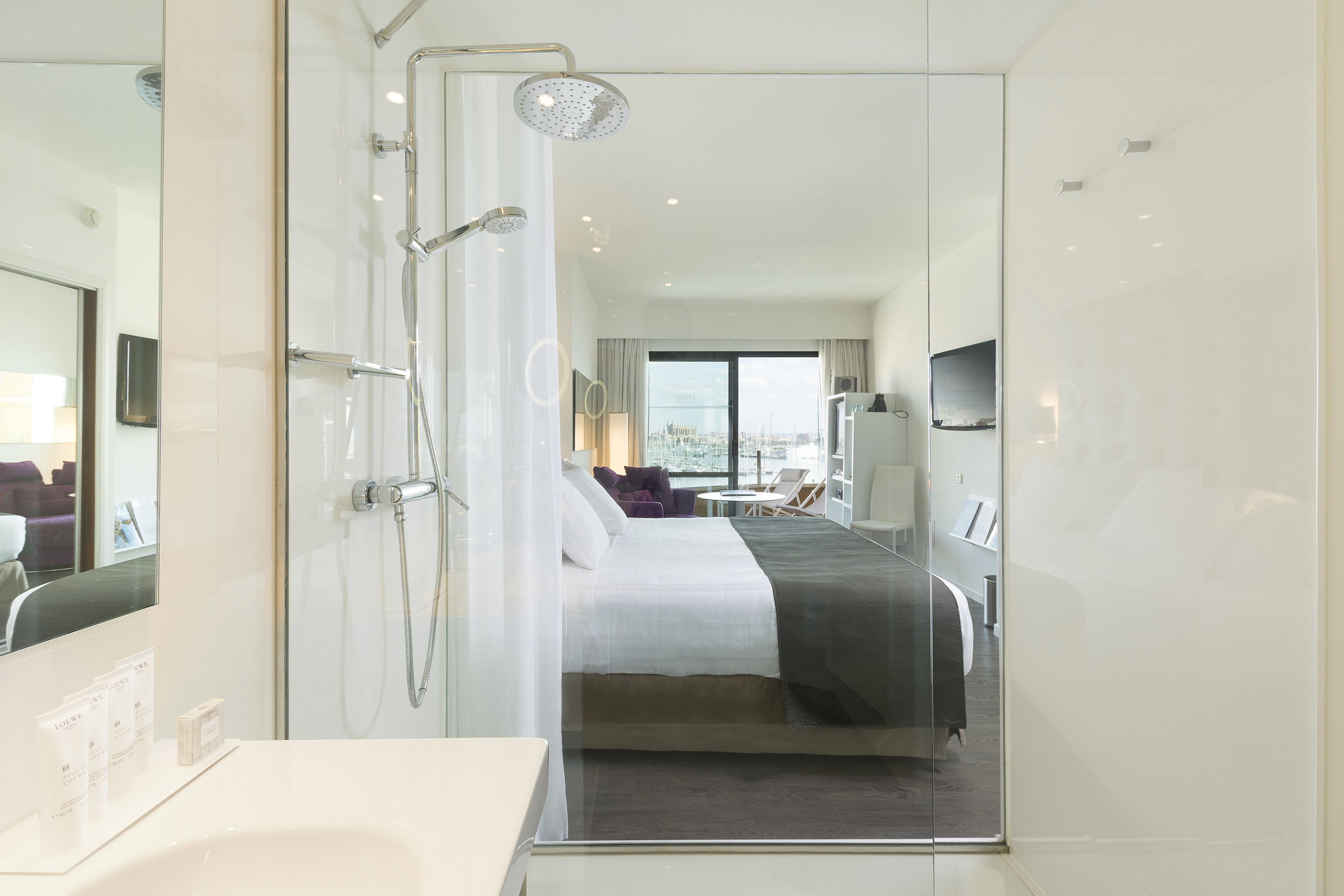 Luxury hotel suite with glass shower, bed, and marina view.