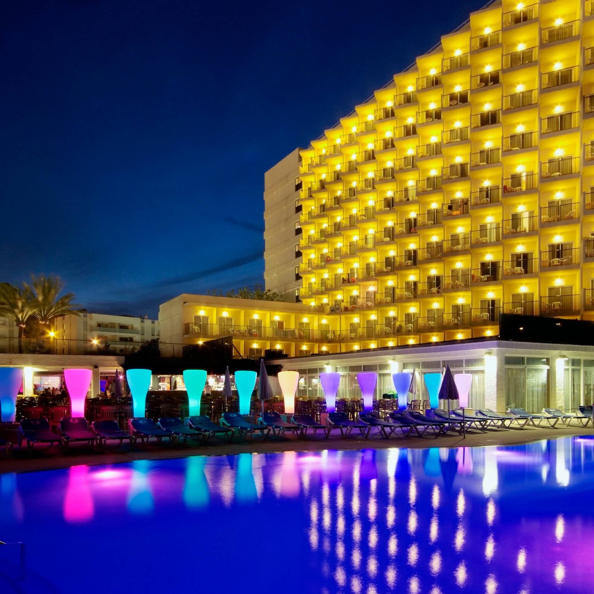 a pool with colorful lights and a building in the background
