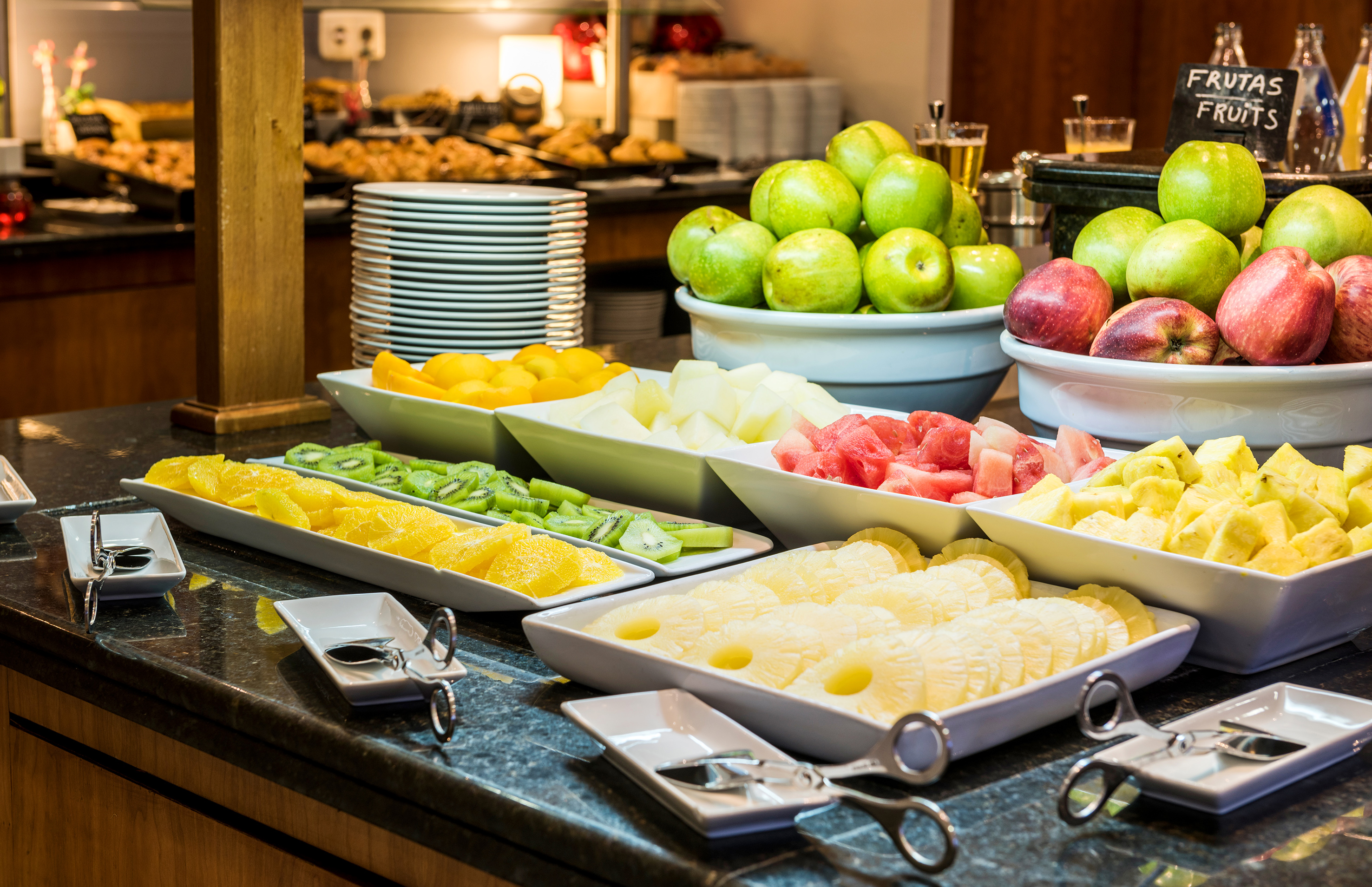 Fresh fruit buffet with sliced pineapple, watermelon, kiwi, oranges, and whole apples.