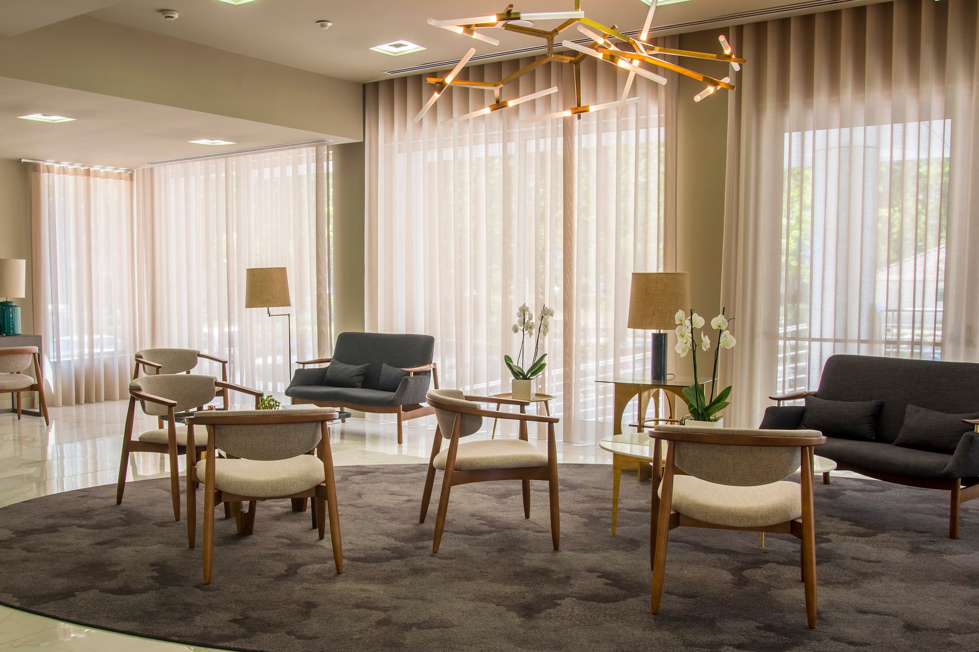 Modern lounge interior with stylish seating, sheer curtains, and geometric chandelier.