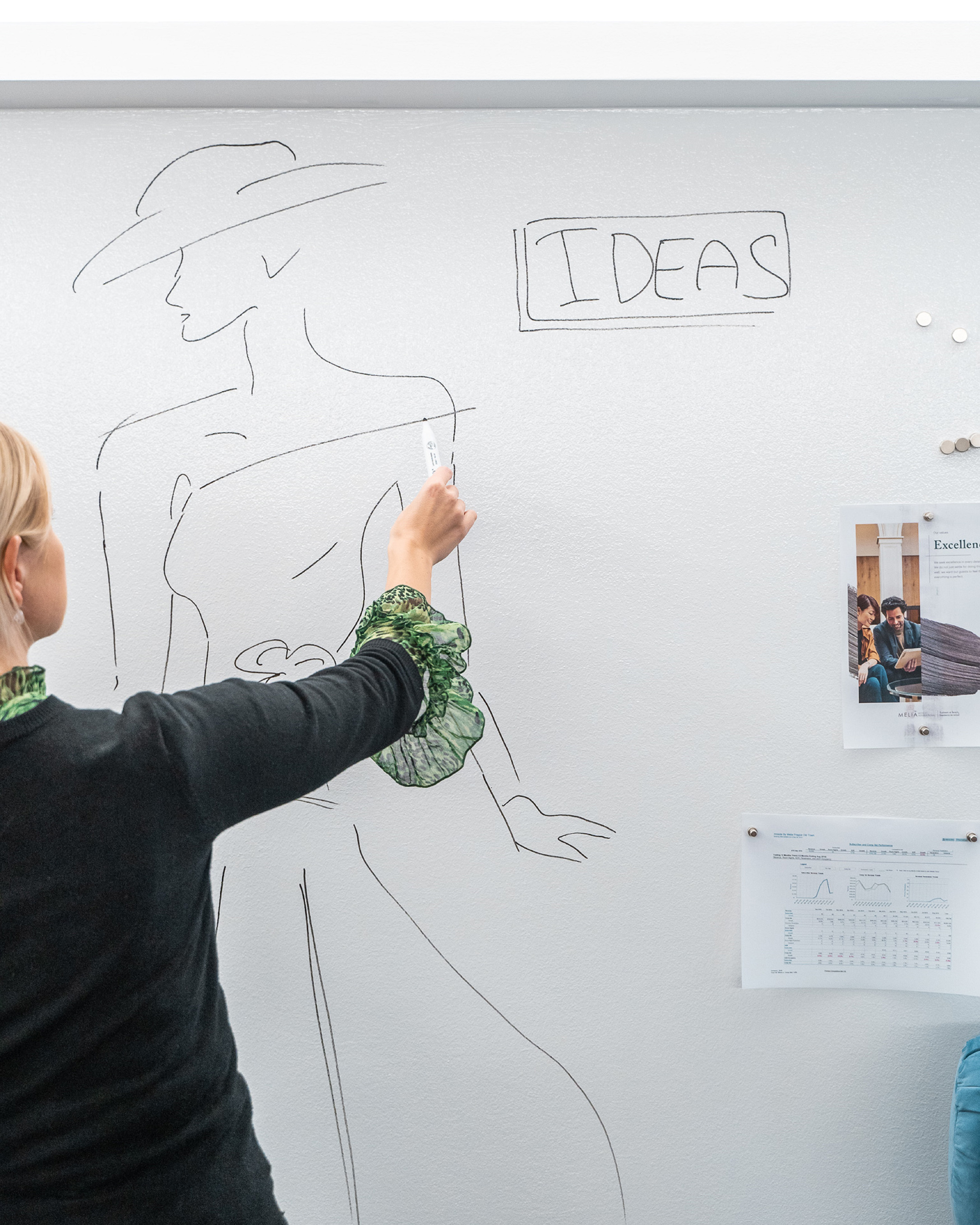 Woman sketching fashion ideas on a whiteboard with a marker.