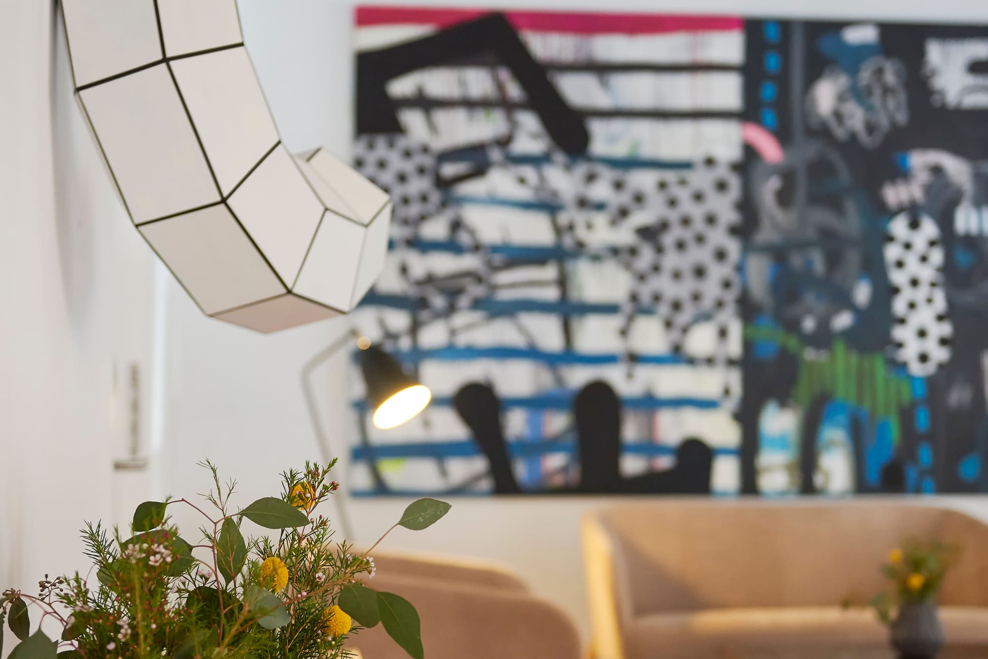 Modern living room with abstract art, geometric wall sculpture, and floral decor.