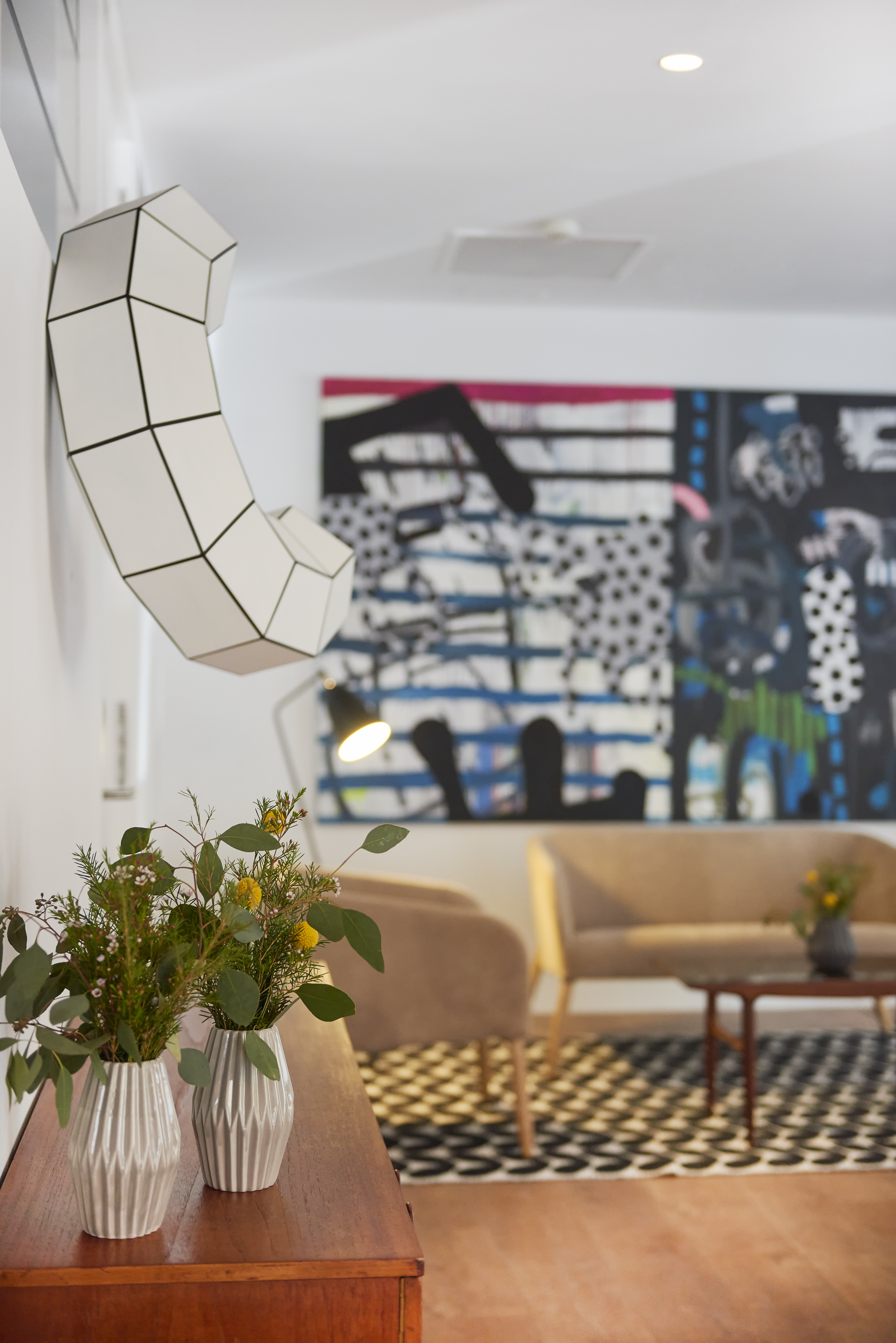 Modern living room with abstract art, geometric wall sculpture, and floral decor.