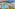 Sunny resort aerial: large pool, beach, palm trees, boats on clear blue ocean.