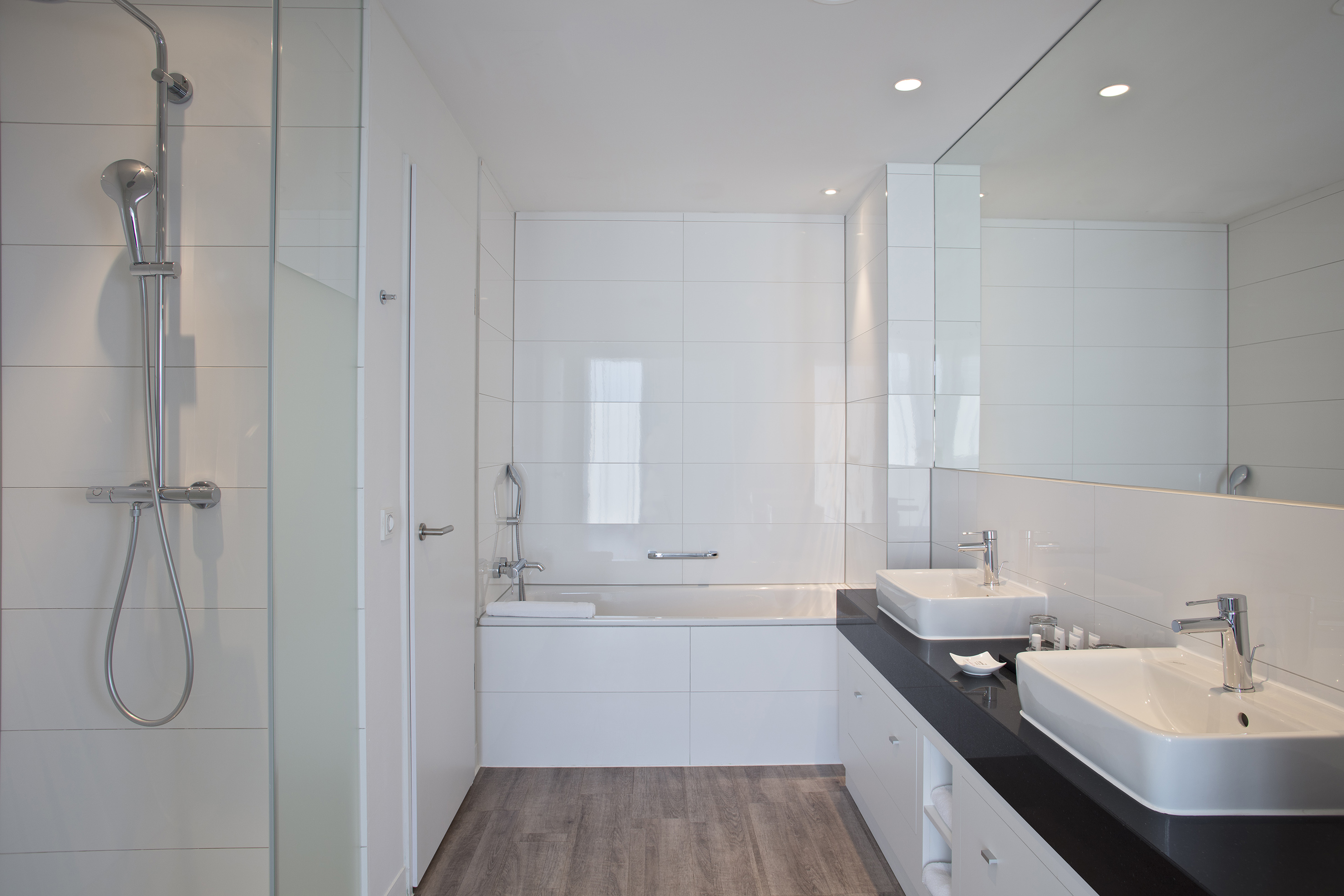 Clean white modern bathroom with shower, bathtub, and black double vanity.