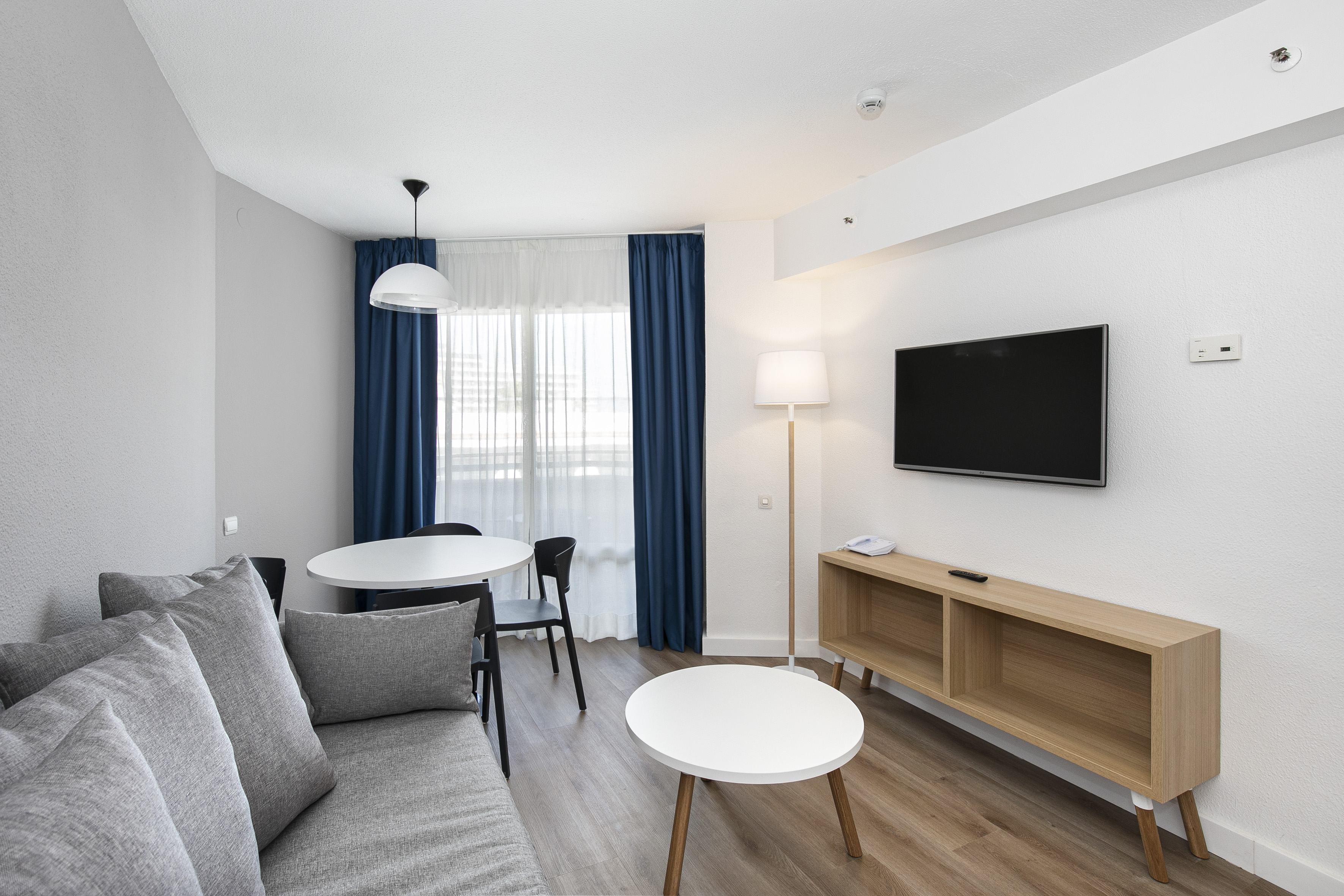 Modern studio apartment living room with gray sofa, dining table, and TV.