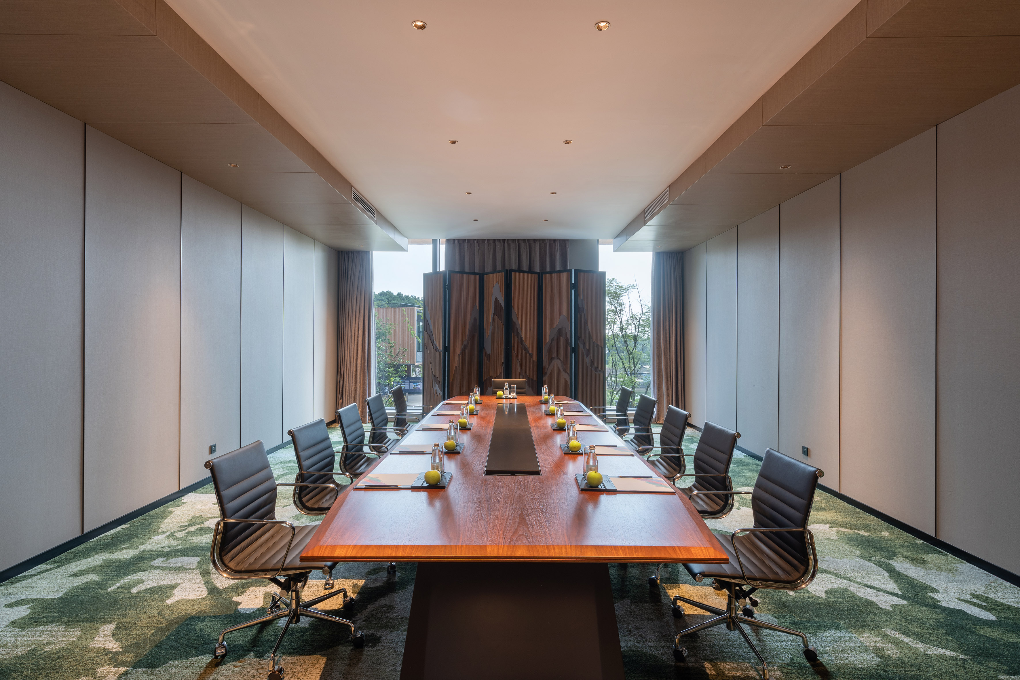 Modern conference room with wooden table, executive chairs, and green carpet.