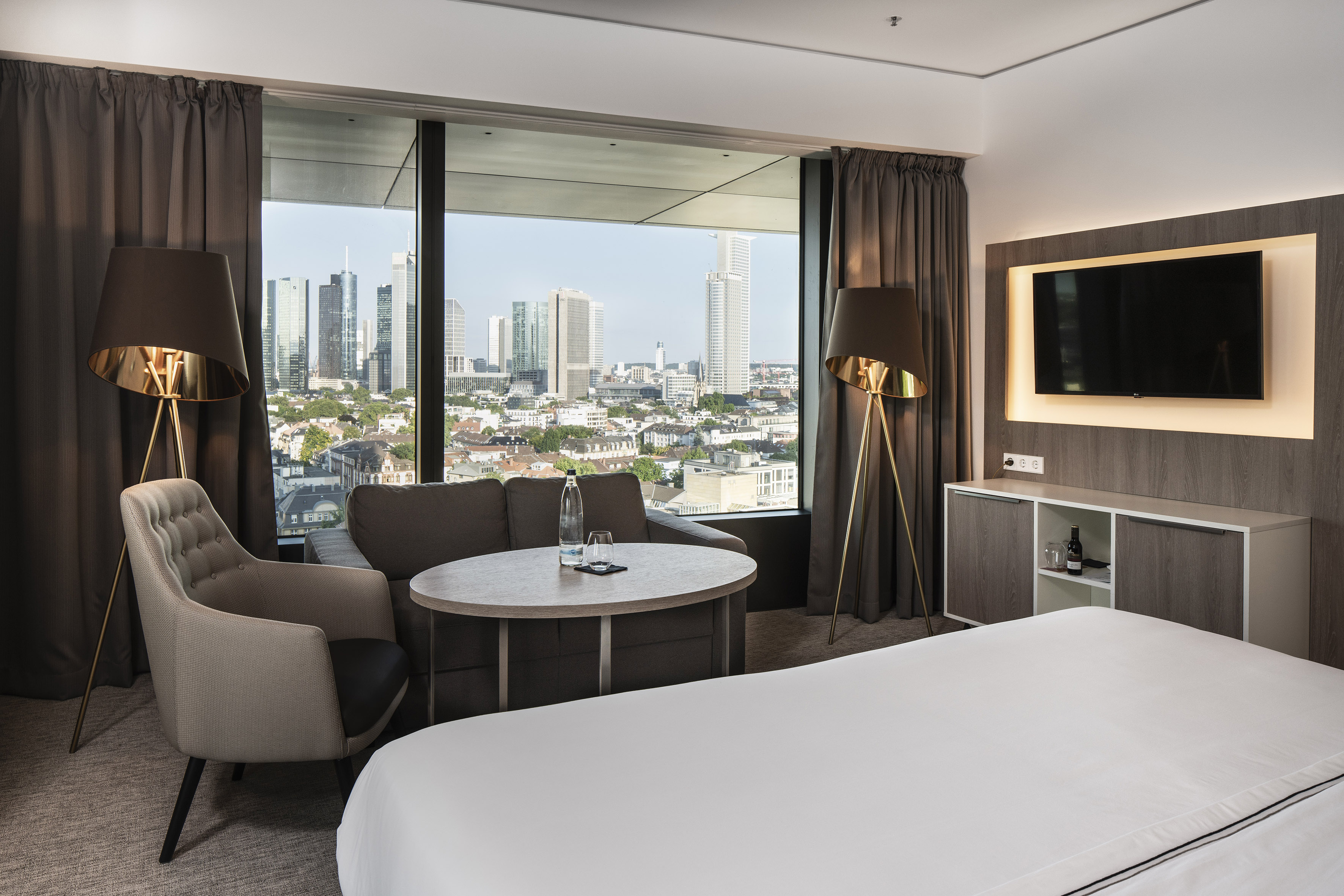 Hotel room with Frankfurt city skyline view, bed, and lounge area.