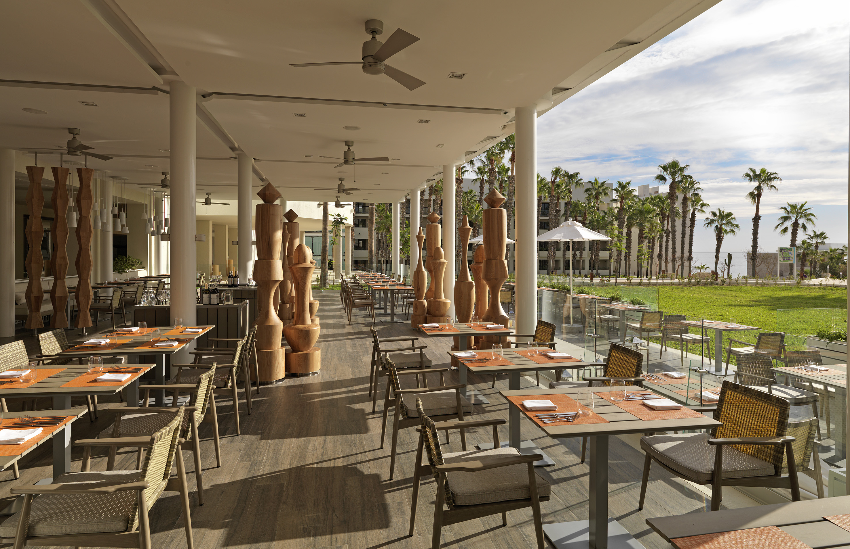 Modern outdoor restaurant with wooden decor, dining tables, and palm trees.