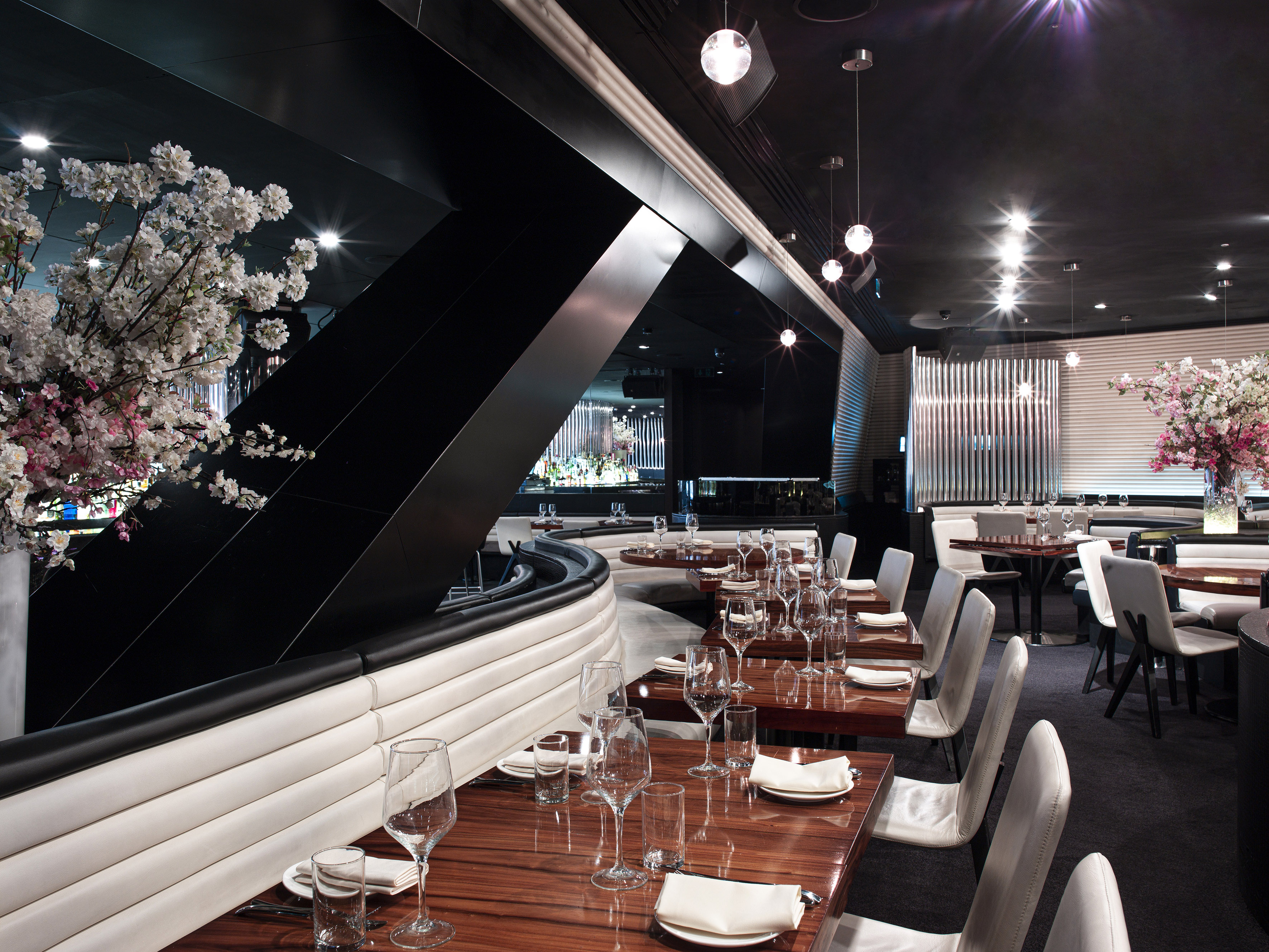 Modern upscale dining room with black, white interior, set tables, and blossoms.