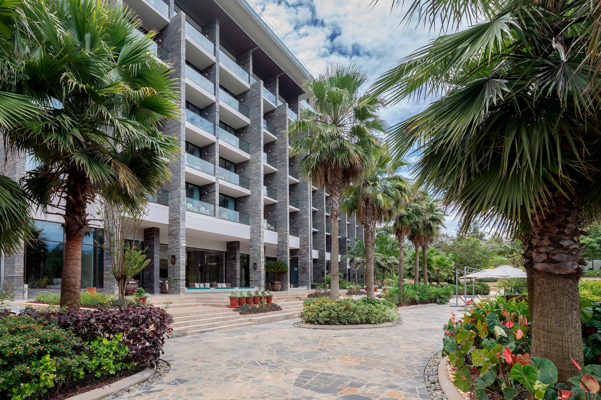 Tropical hotel exterior with palm trees, modern stone facade, and balconies.