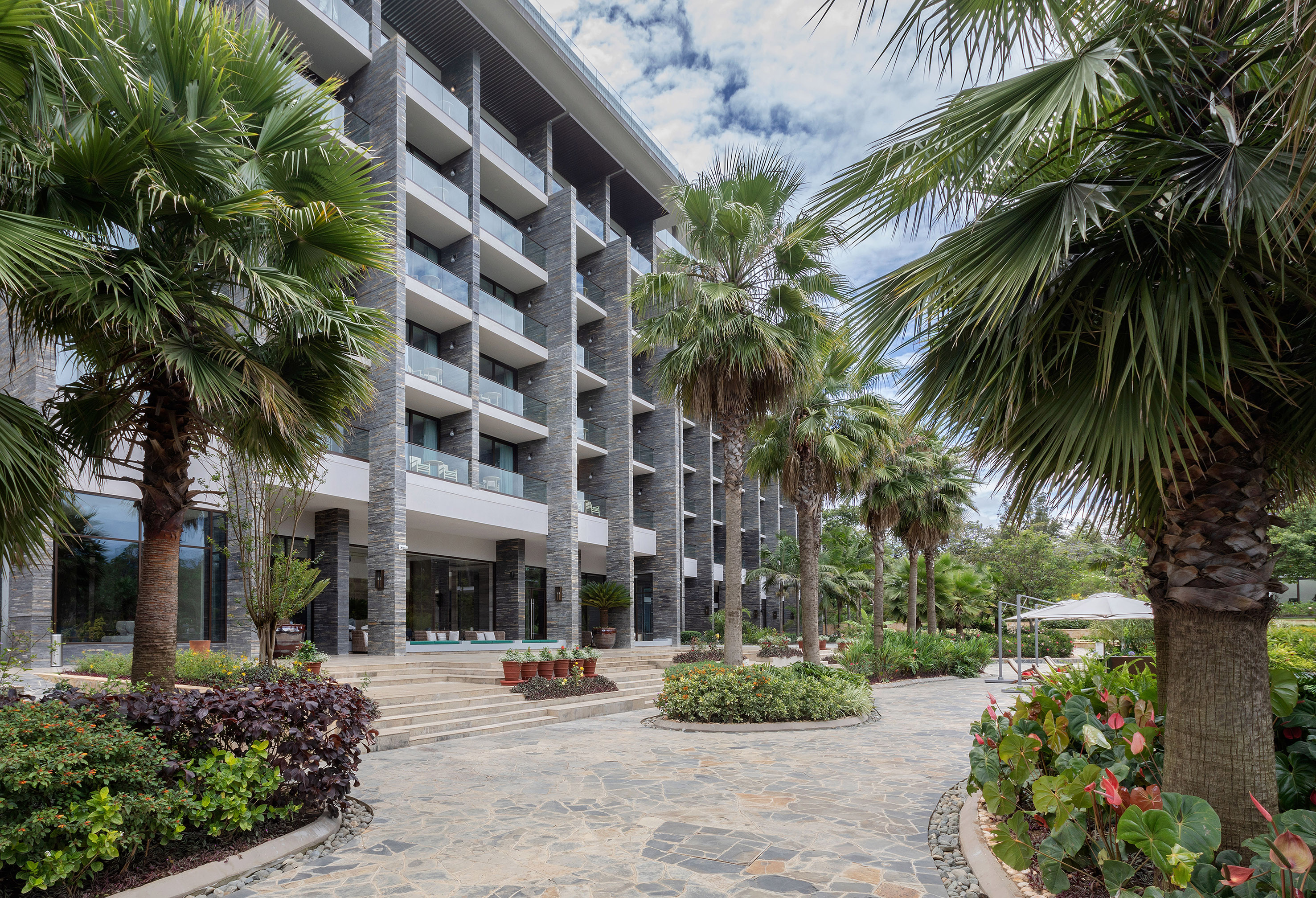 Tropical hotel exterior with palm trees, modern stone facade, and balconies.