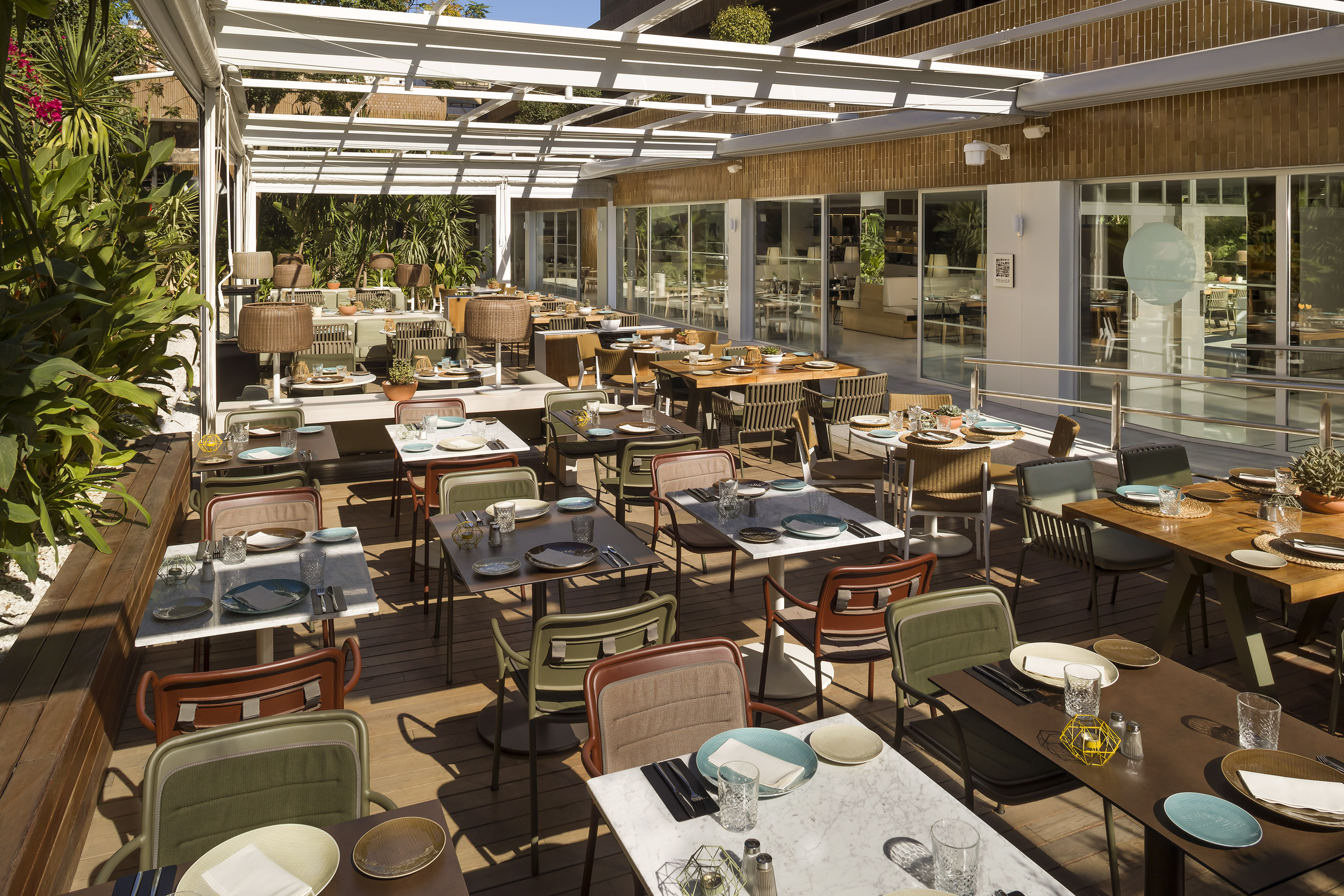 Modern outdoor restaurant patio with many tables set for dining under a white trellis.