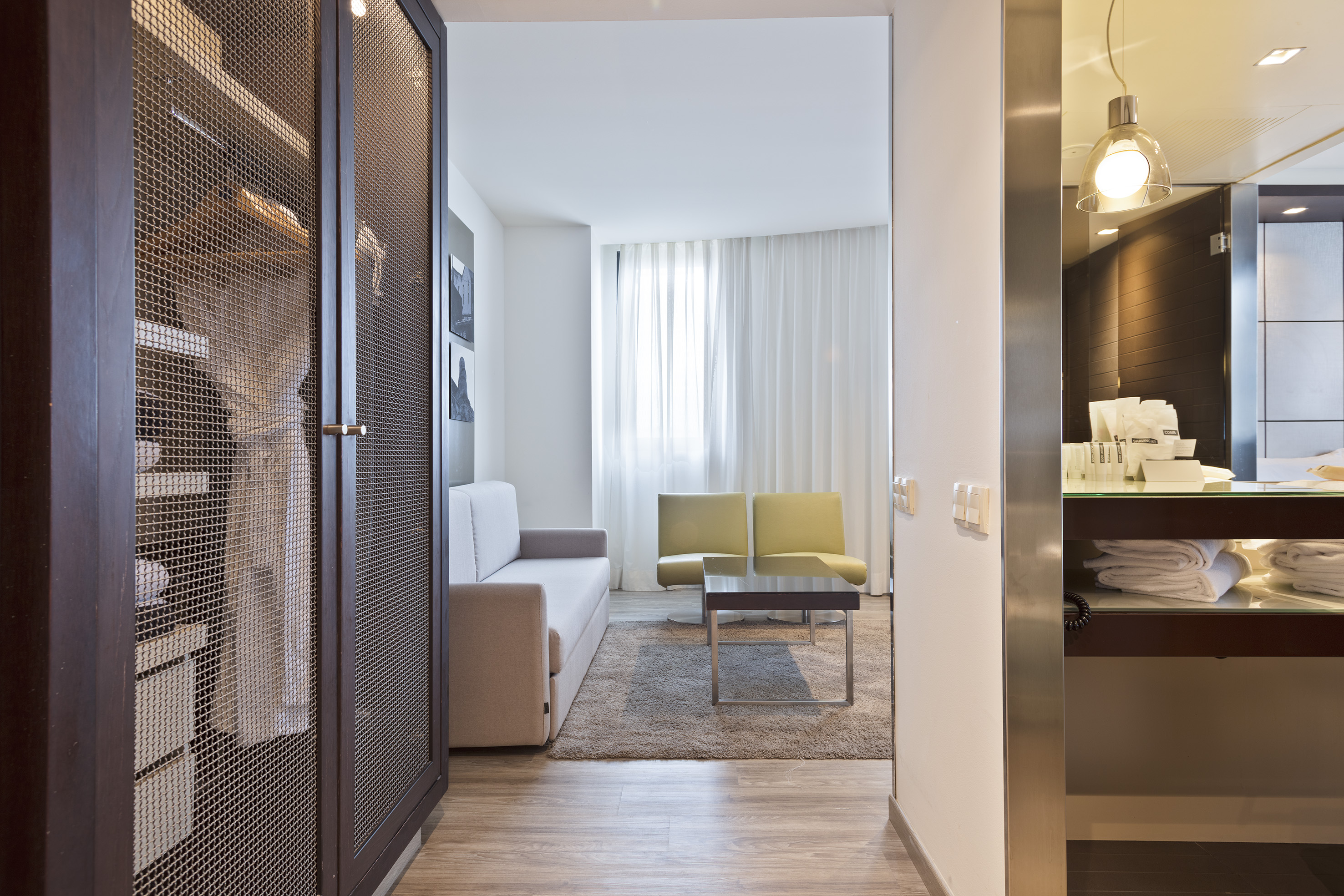 Hotel suite entryway with mesh wardrobe, light living room, and vanity counter.
