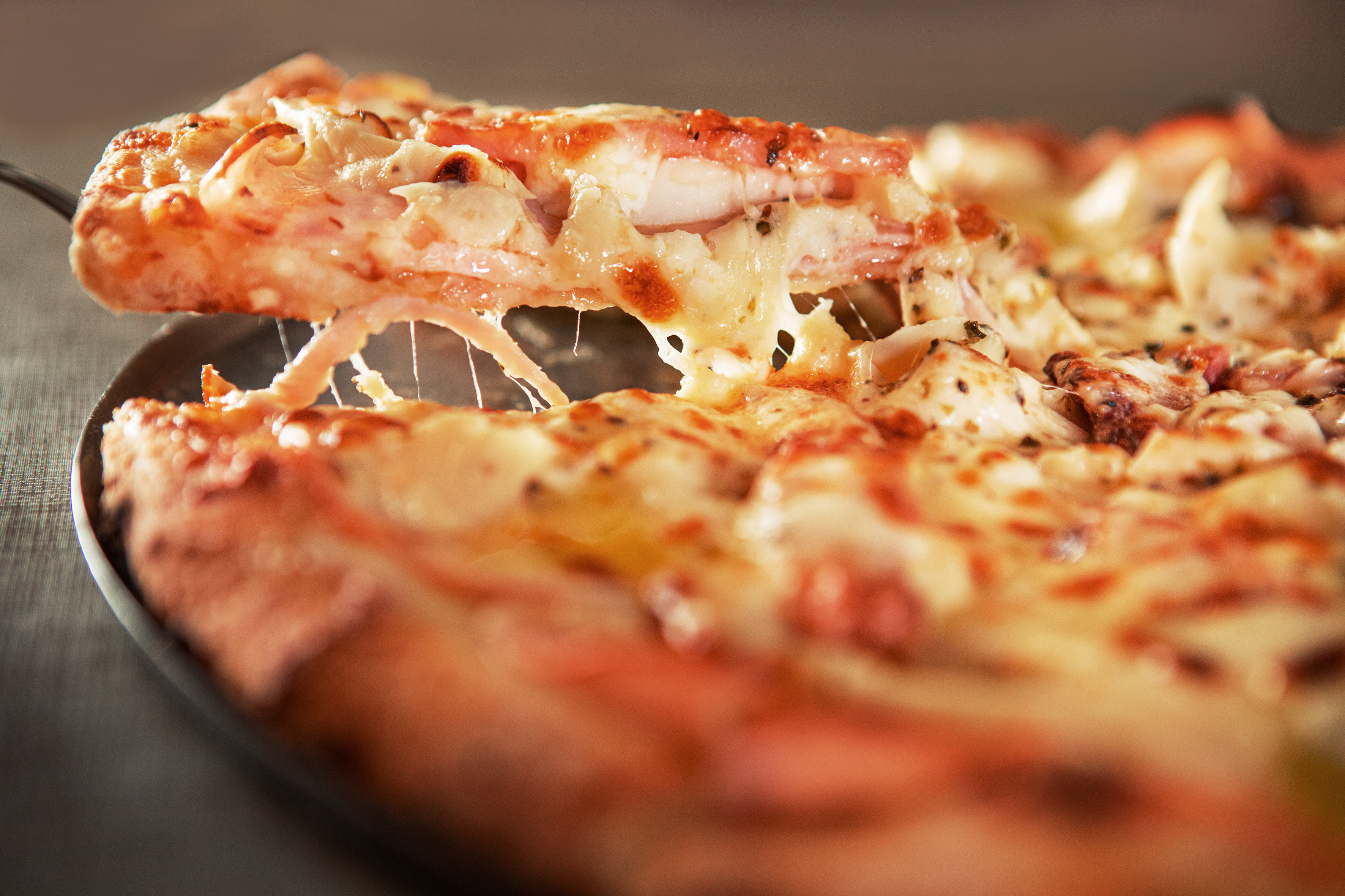 Hot pizza slice with gooey melted cheese stretching as it's lifted.