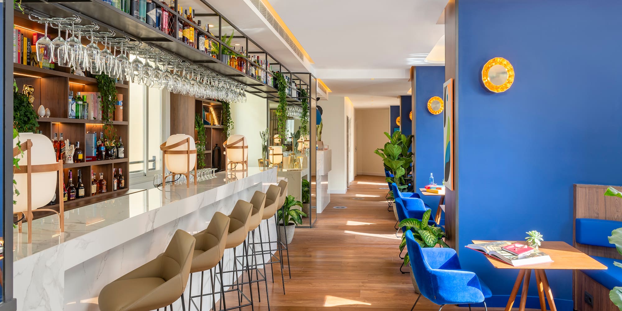 Stylish modern hotel bar with marble counter, liquor display, and blue lounge seating.