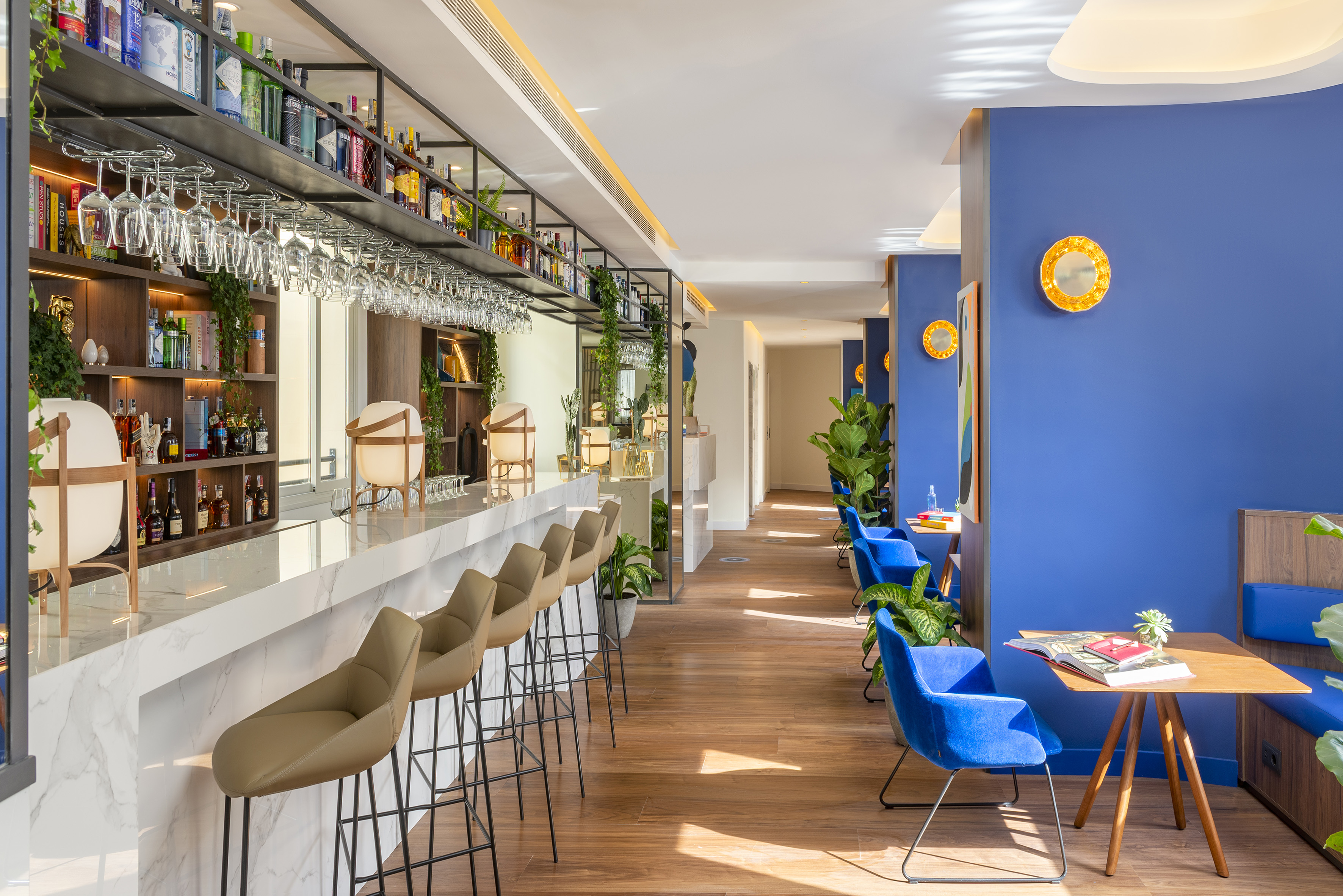 Stylish modern hotel bar with marble counter, liquor display, and blue lounge seating.