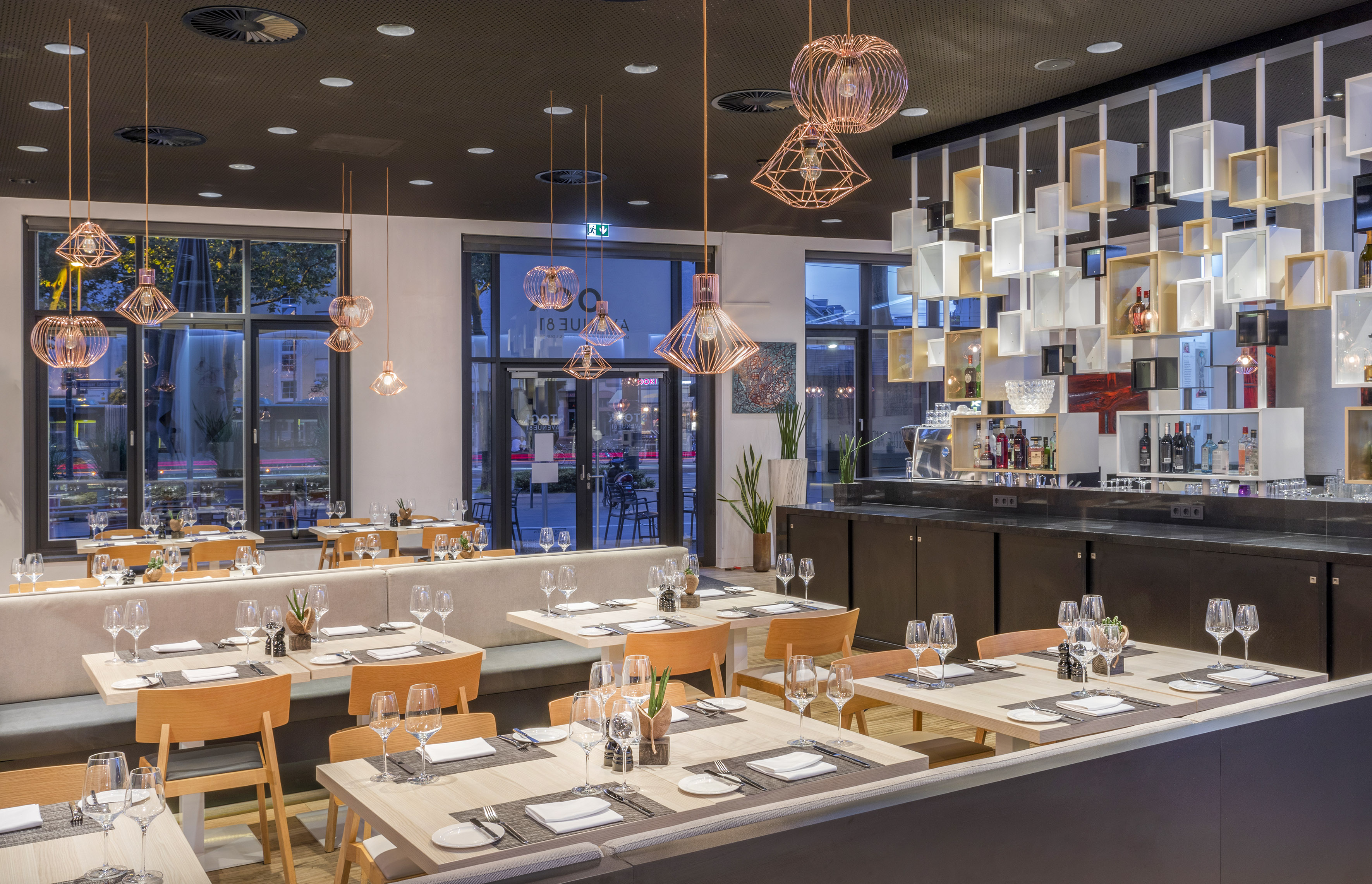 Contemporary restaurant interior with set tables, pendant lights, and bar.