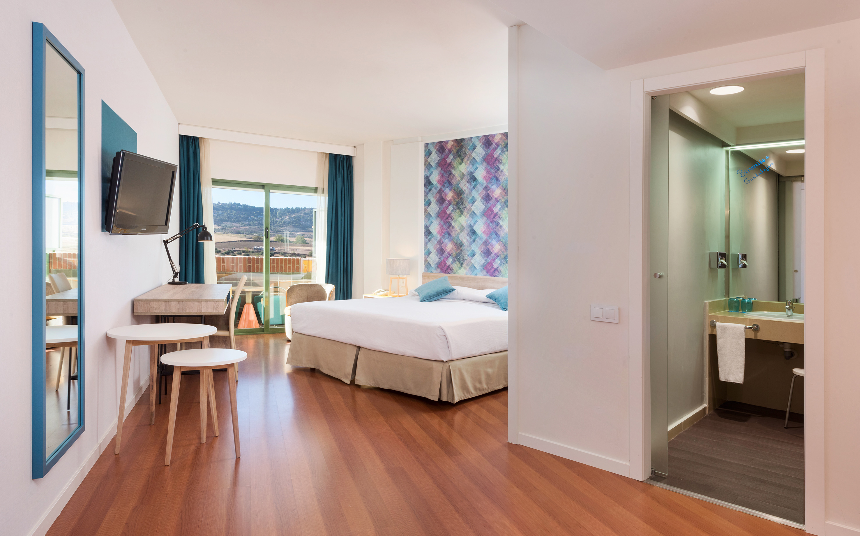 Contemporary hotel suite with king bed, desk, balcony, and en-suite bathroom.