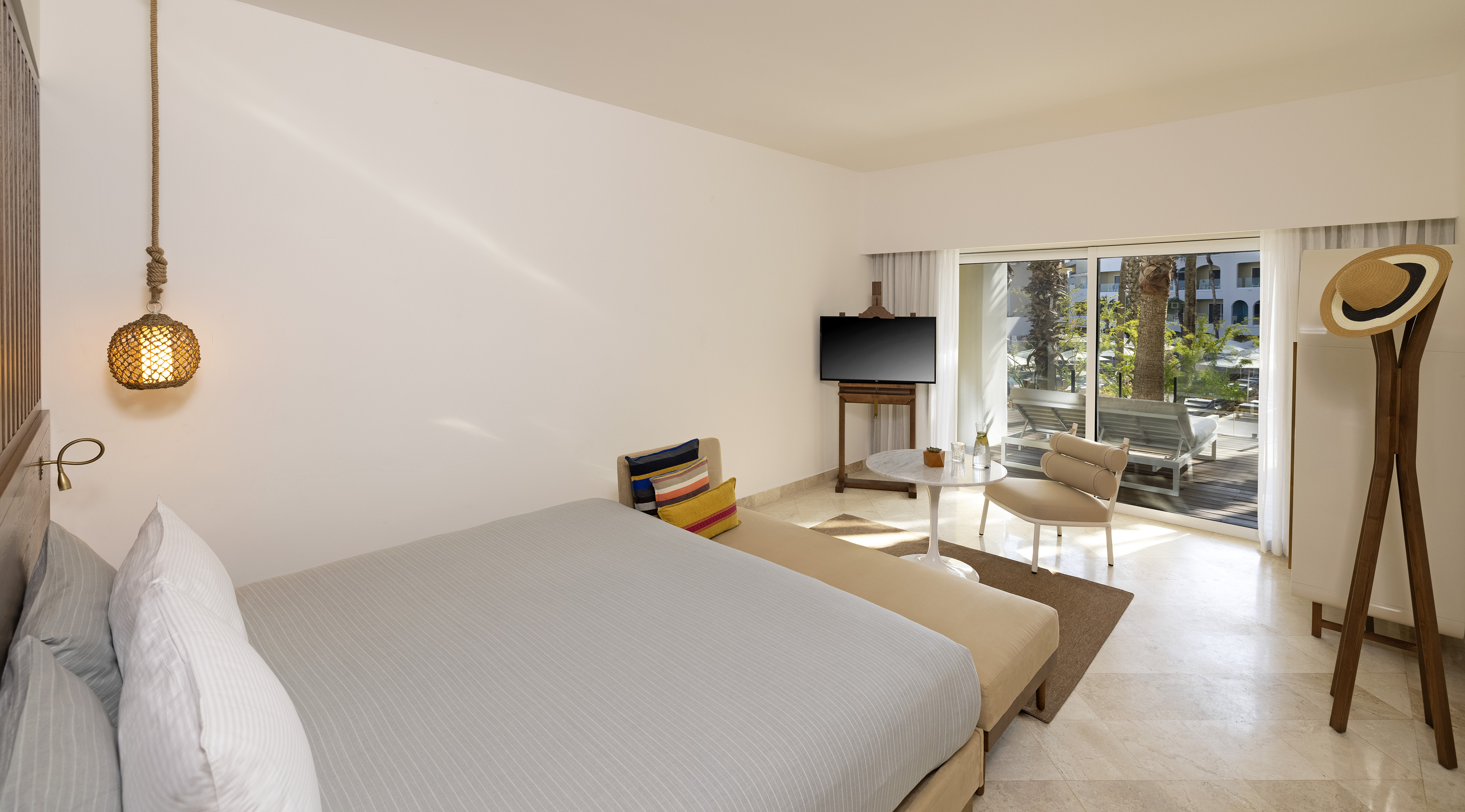 Modern hotel room with king bed, balcony, and tropical resort view.