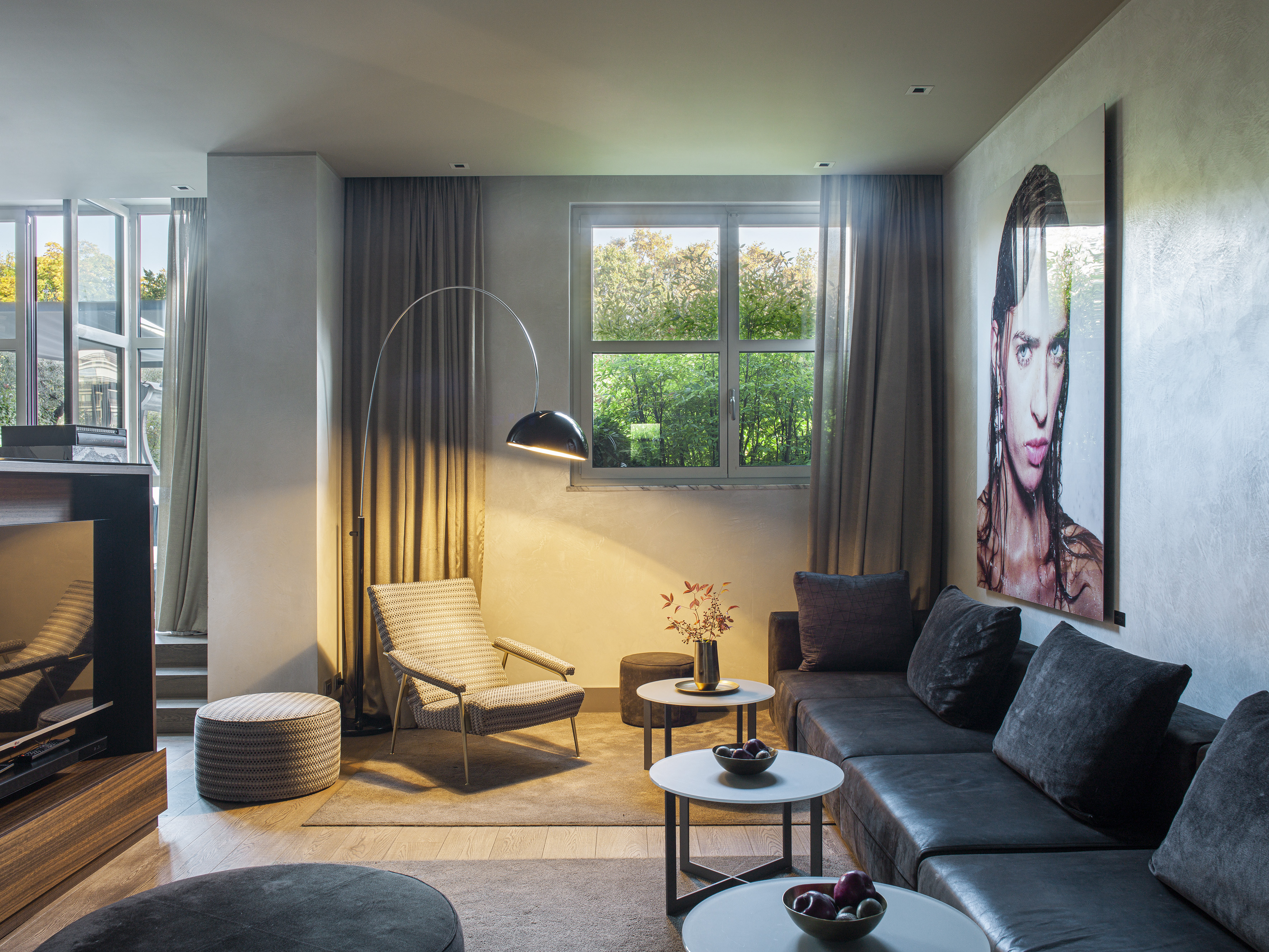Modern living room with dark sectional sofa, window, arc lamp, and large wall art.