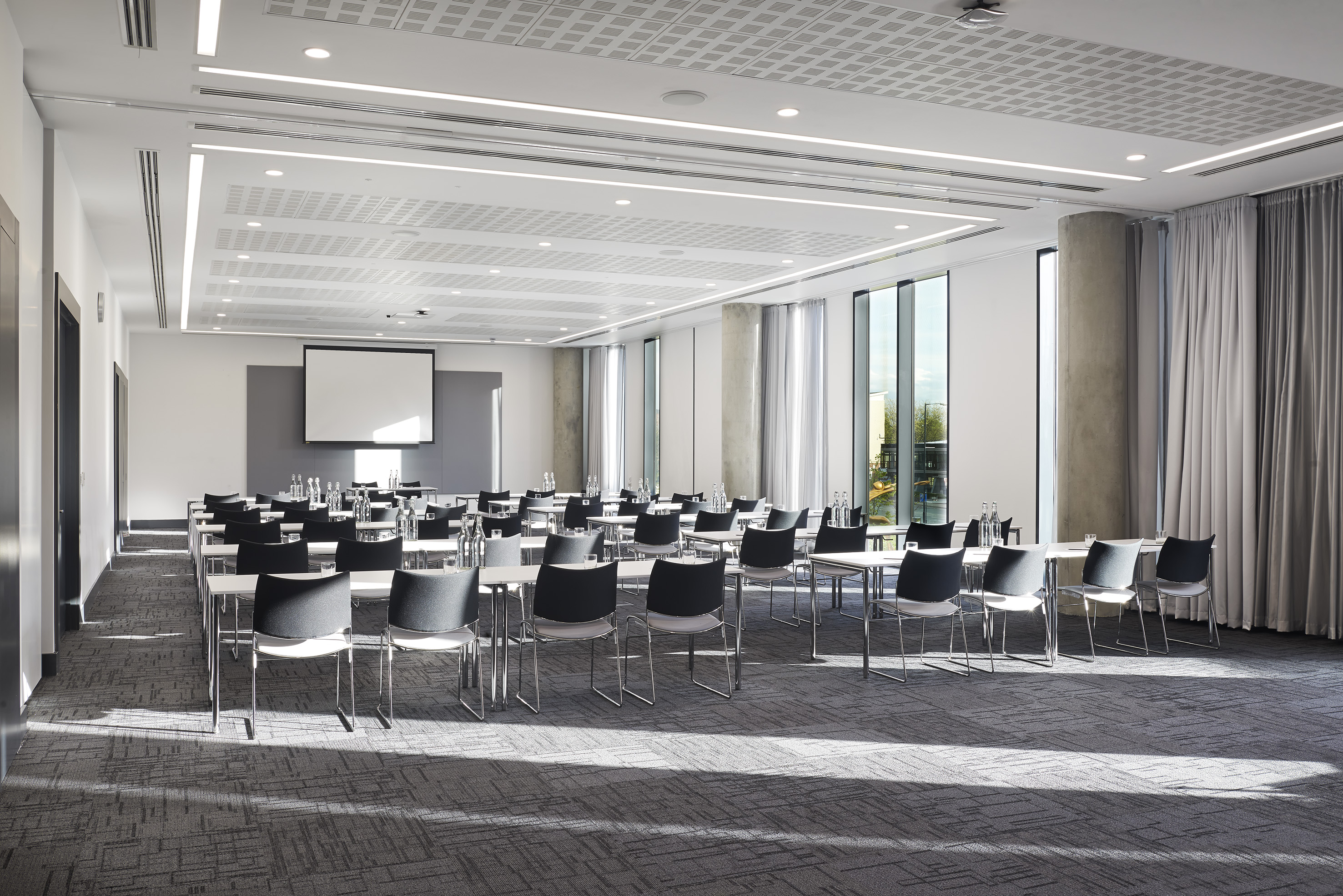 Empty modern training room, classroom style setup, projector screen, daylight.