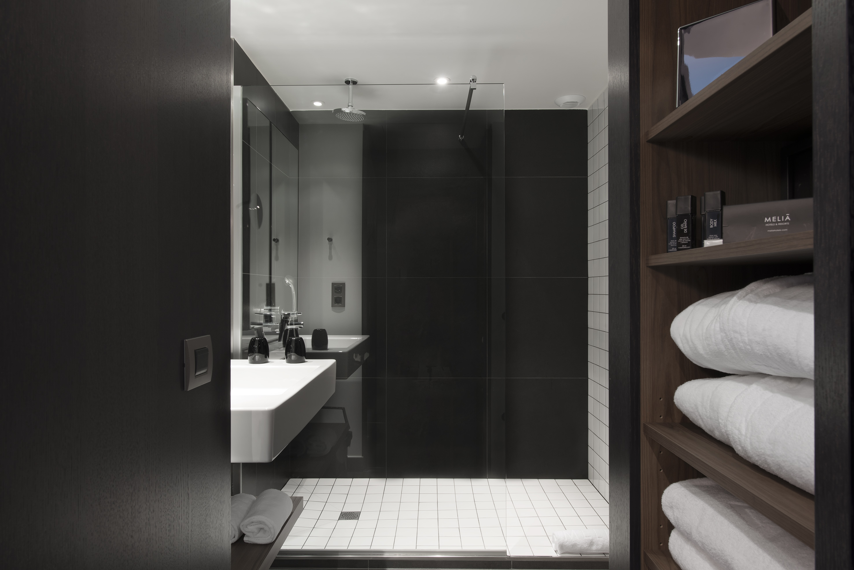Modern Meliá bathroom with dark shower, white vanity, and fresh towels.